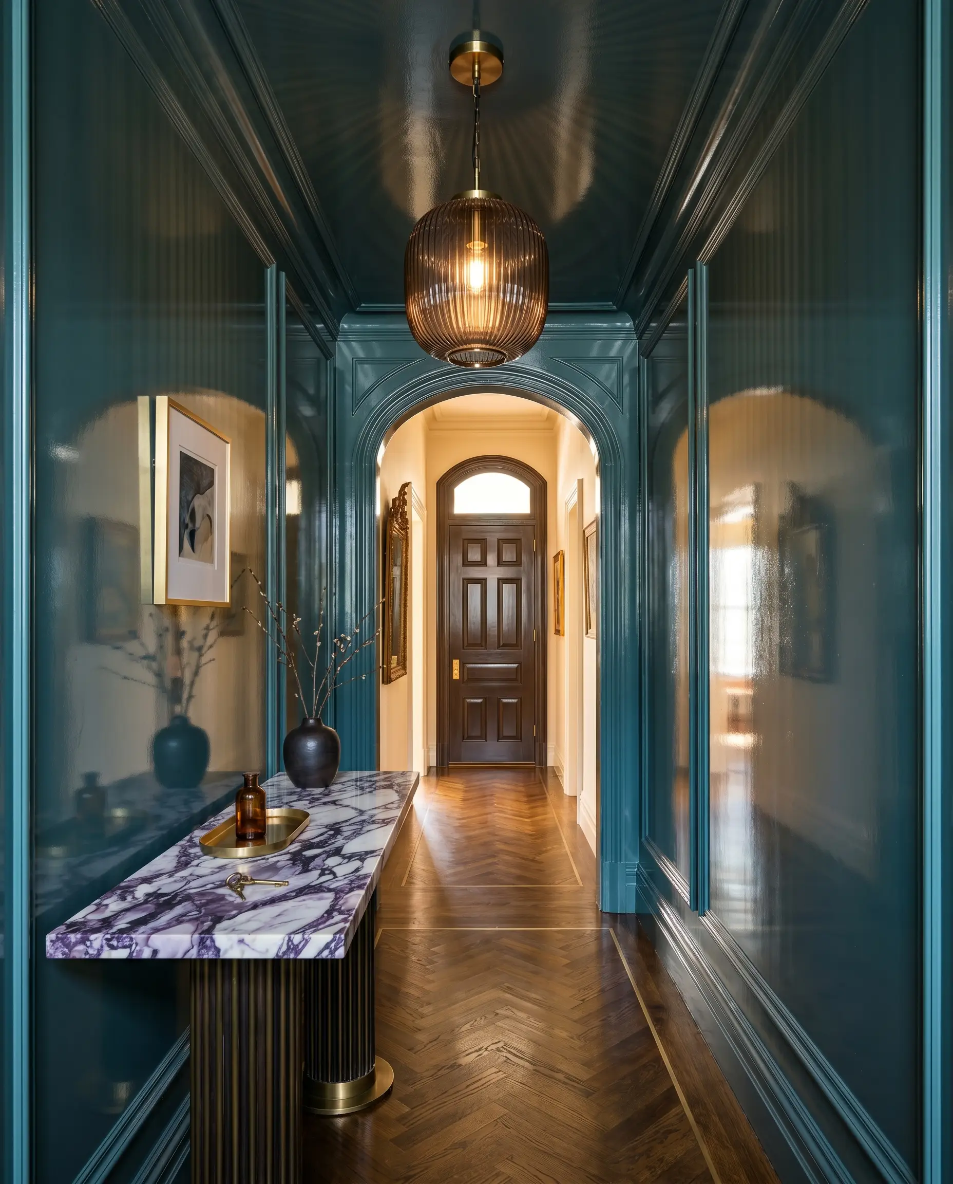 A Calacatta Viola marble console table and a smoked ribbed glass pendant light sit within a narrow transitional vestibule finished in high-gloss rich teal paint.