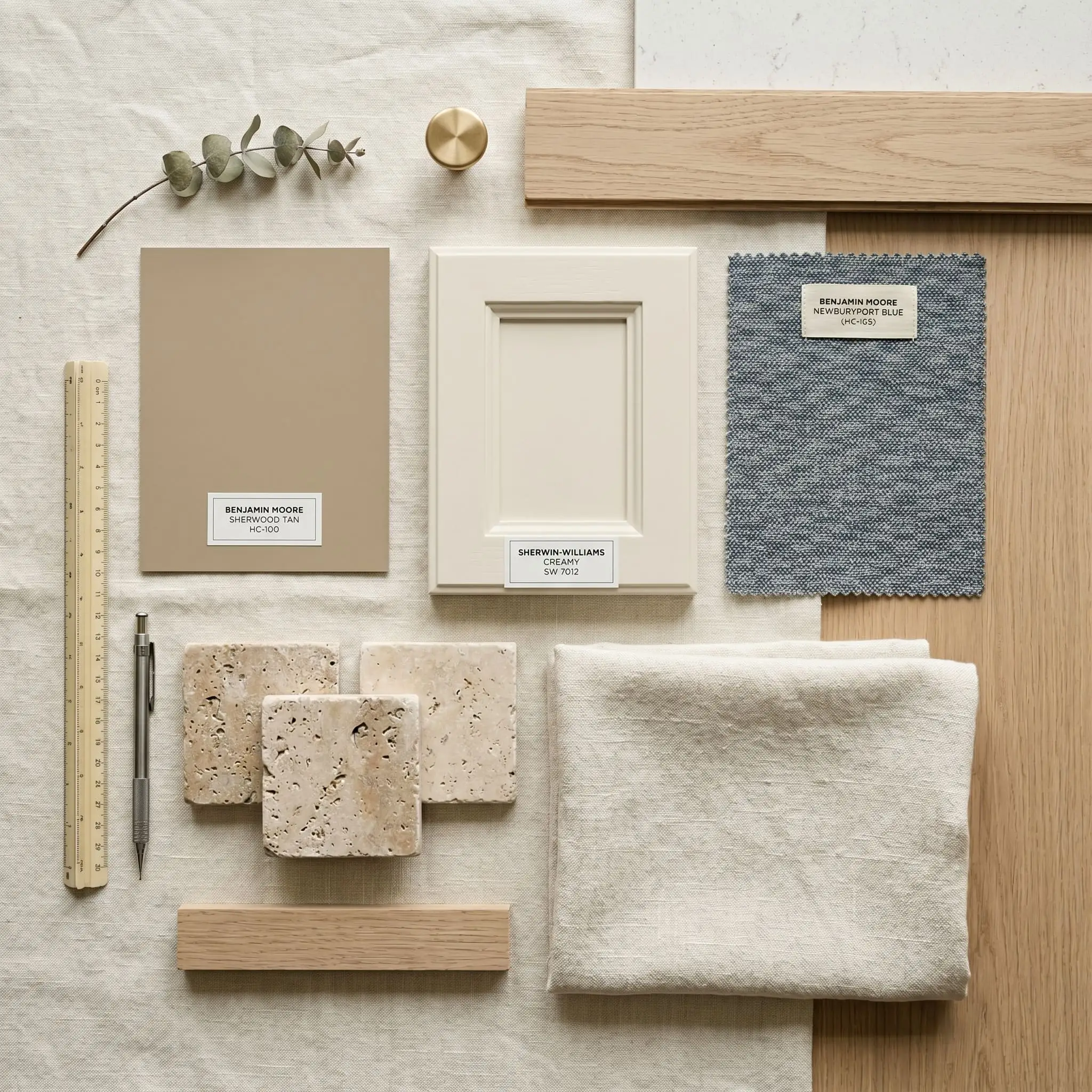 Even diffused studio lighting captures a material moodboard combining tumbled travertine stone, cream linen fabric, a warm tan paint swatch, and navy blue accents.