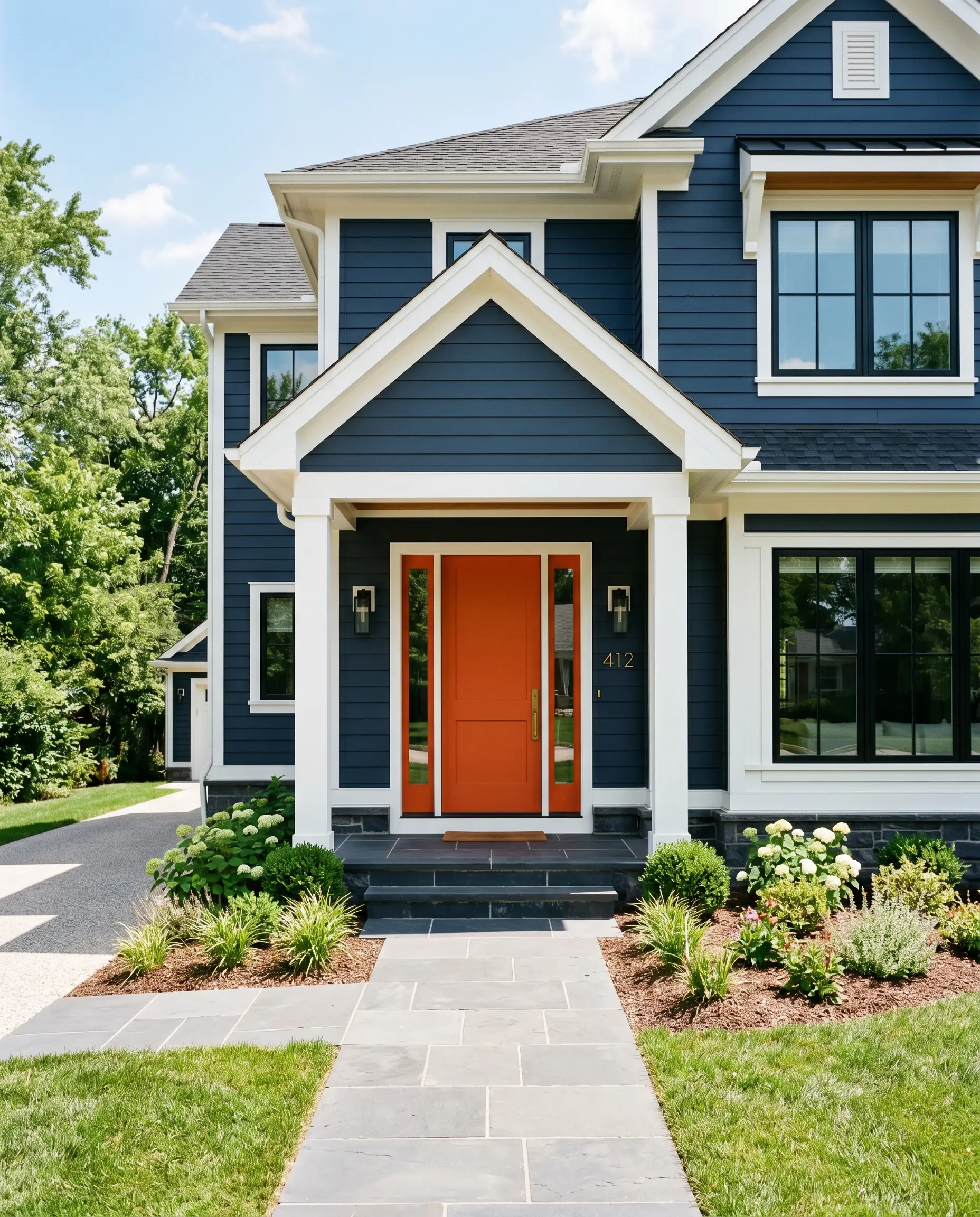 A vivid warm orange semi-gloss front door contrasts sharply against deep navy siding, crisp white architectural trim, and a honed black basalt porch step.