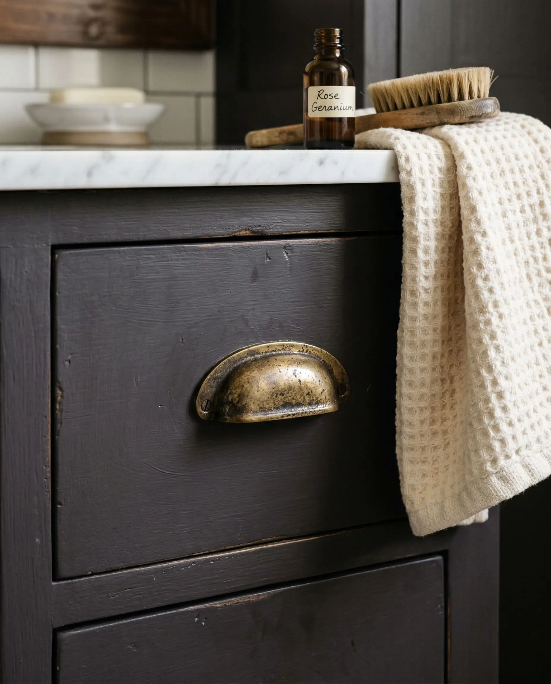 The cold, heavy bite of an unlacquered brass drawer pull cuts sharply through the cool violet undertones of a smooth, dark vanity cabinet face.