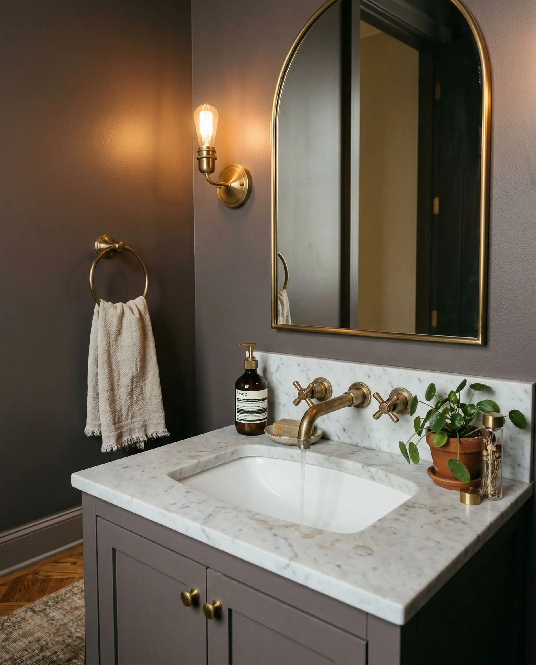 An unlacquered brass faucet is mounted over a marble basin against a rich taupe-gray wall in a transitional modern powder room.