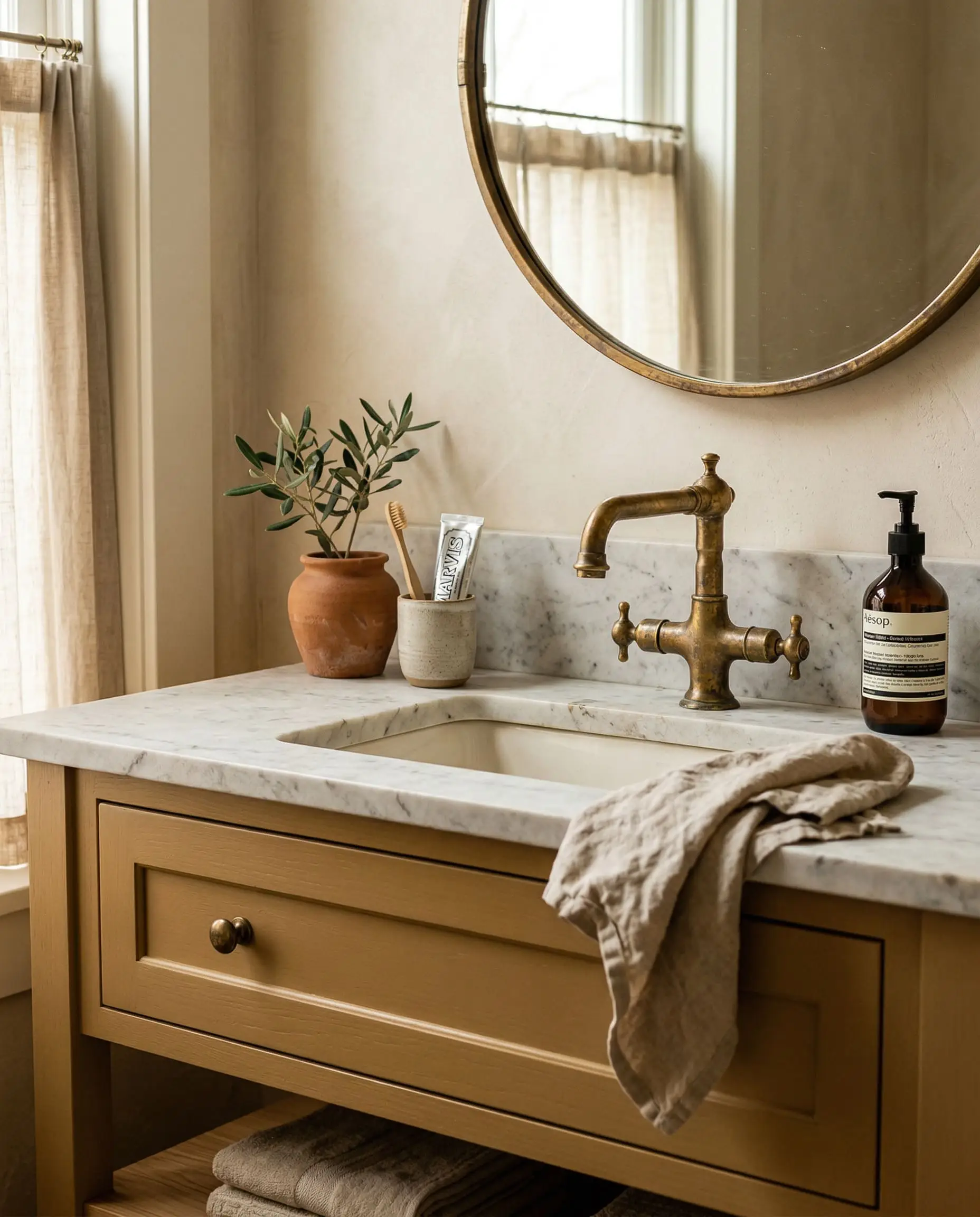 Warm natural light emphasizes the natural patina of an unlacquered brass faucet mounted against a golden-brown painted bathroom vanity surface.
