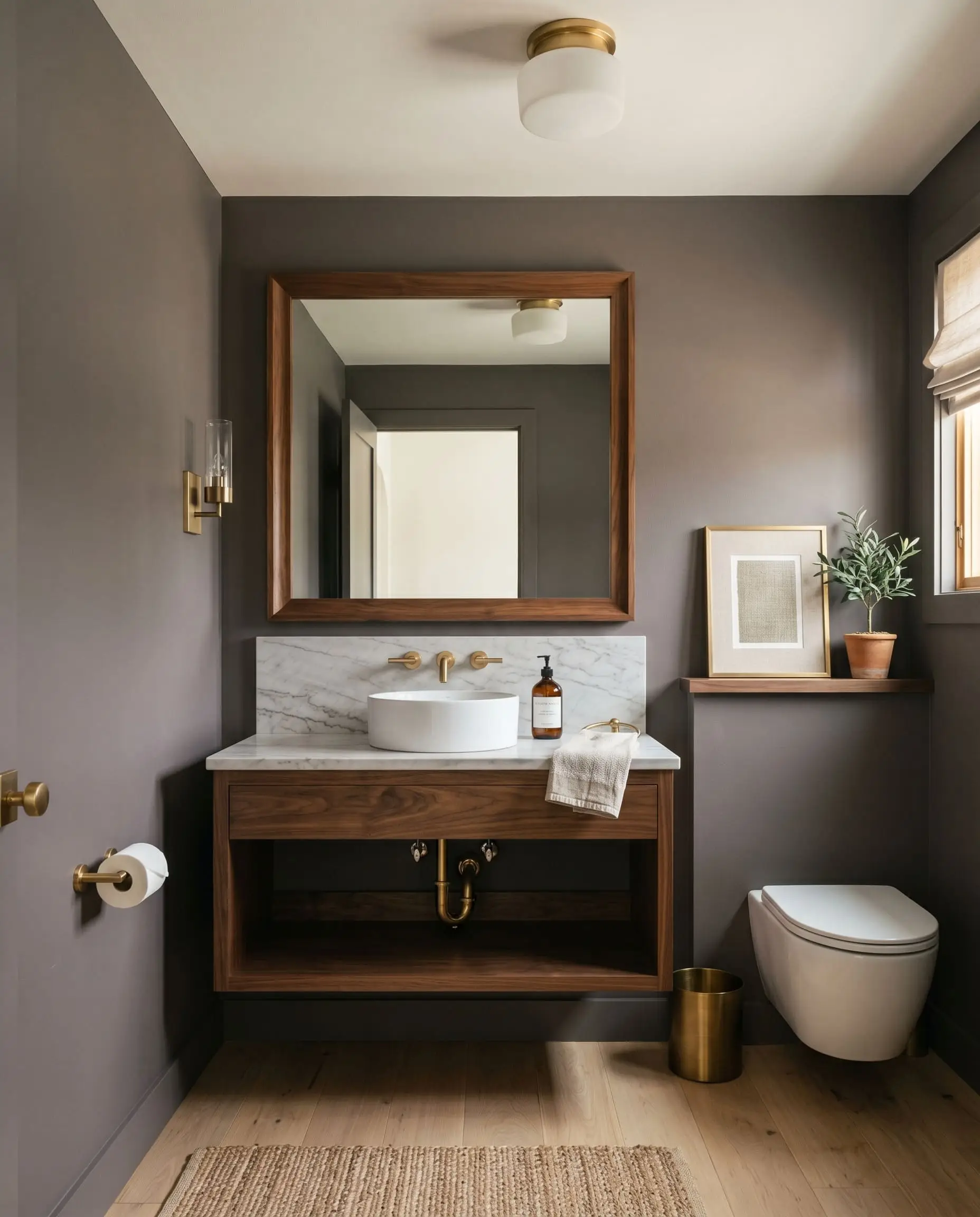 A warm walnut wood mirror frame hangs above neutral white oak floors in a minimalist powder room with deep plum-gray walls.