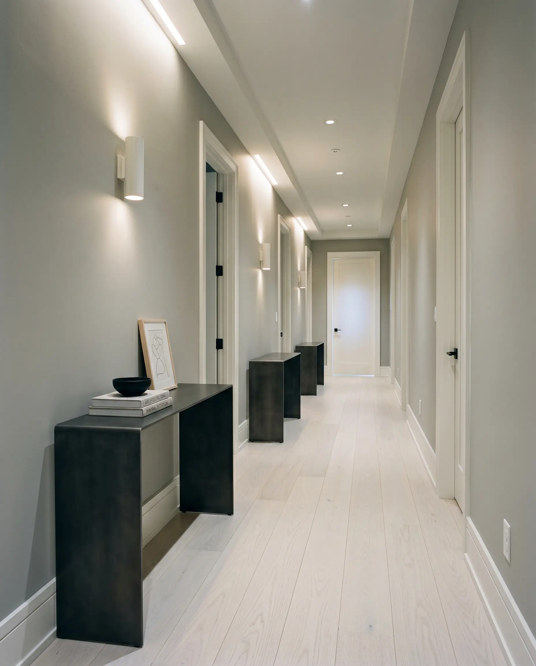 A windowless transitional hallway features crisp walls painted in Farrow & Ball Dimpse (Hex #d4d4d2), white-washed ash wood flooring, and a sleek minimalist cold-rolled steel console table.