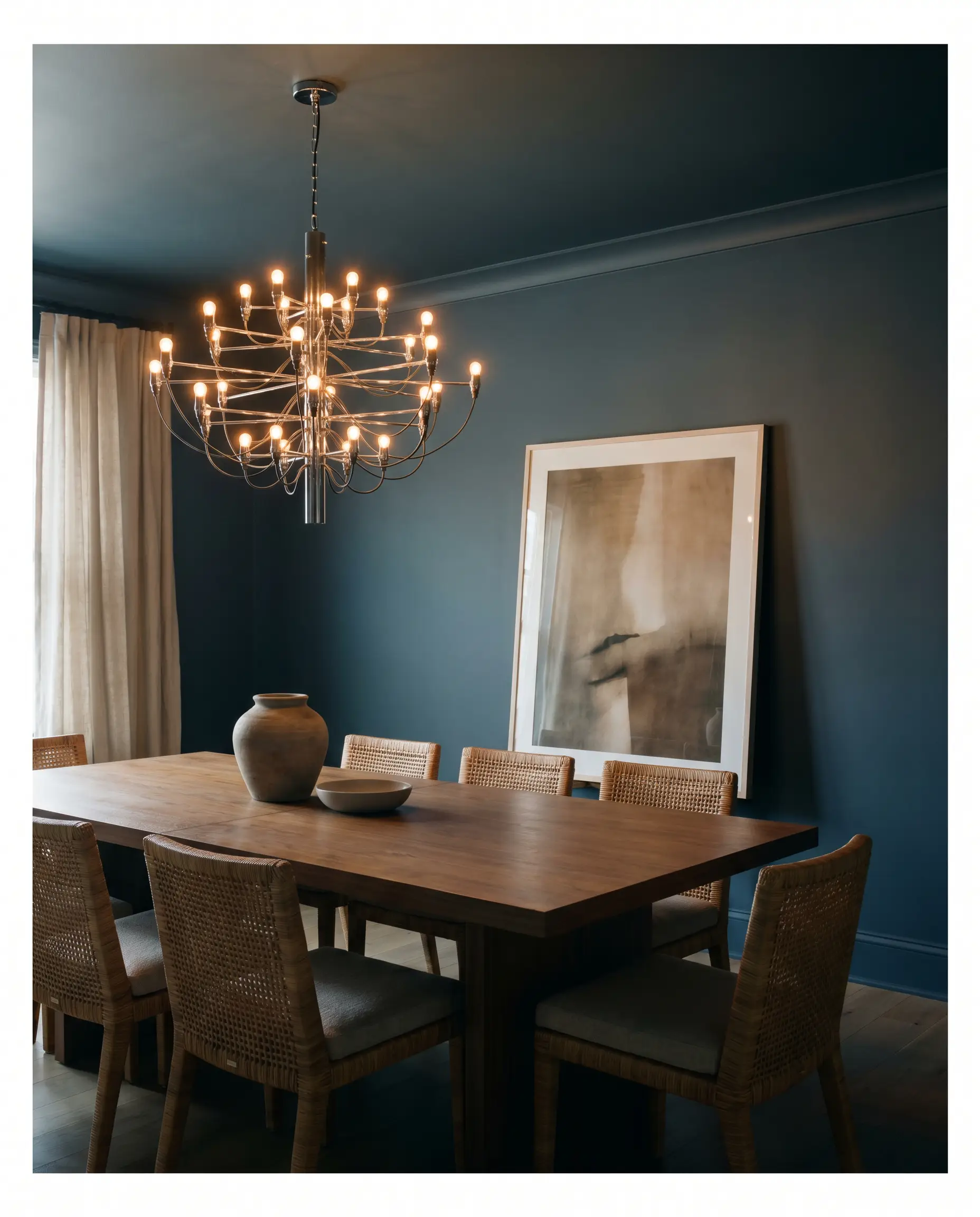 An intimate formal dining room is entirely wrapped in Behr Midnight Blue (Hex #4c565e), framing a medium-dark walnut dining table and woven rattan chairs.