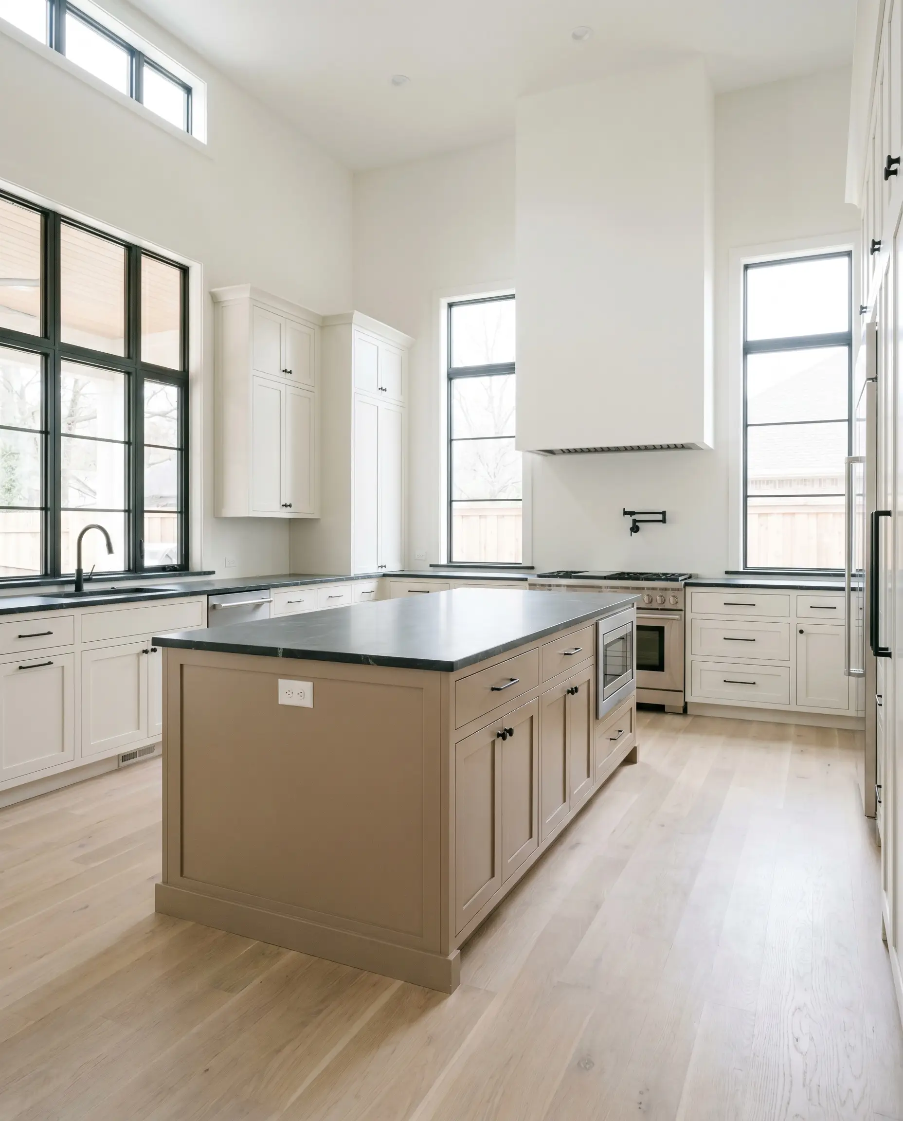 A custom kitchen features perimeter cabinetry in Alabaster and a central island painted in Behr Mocha Foam (Hex #bba28e) topped with honed soapstone.