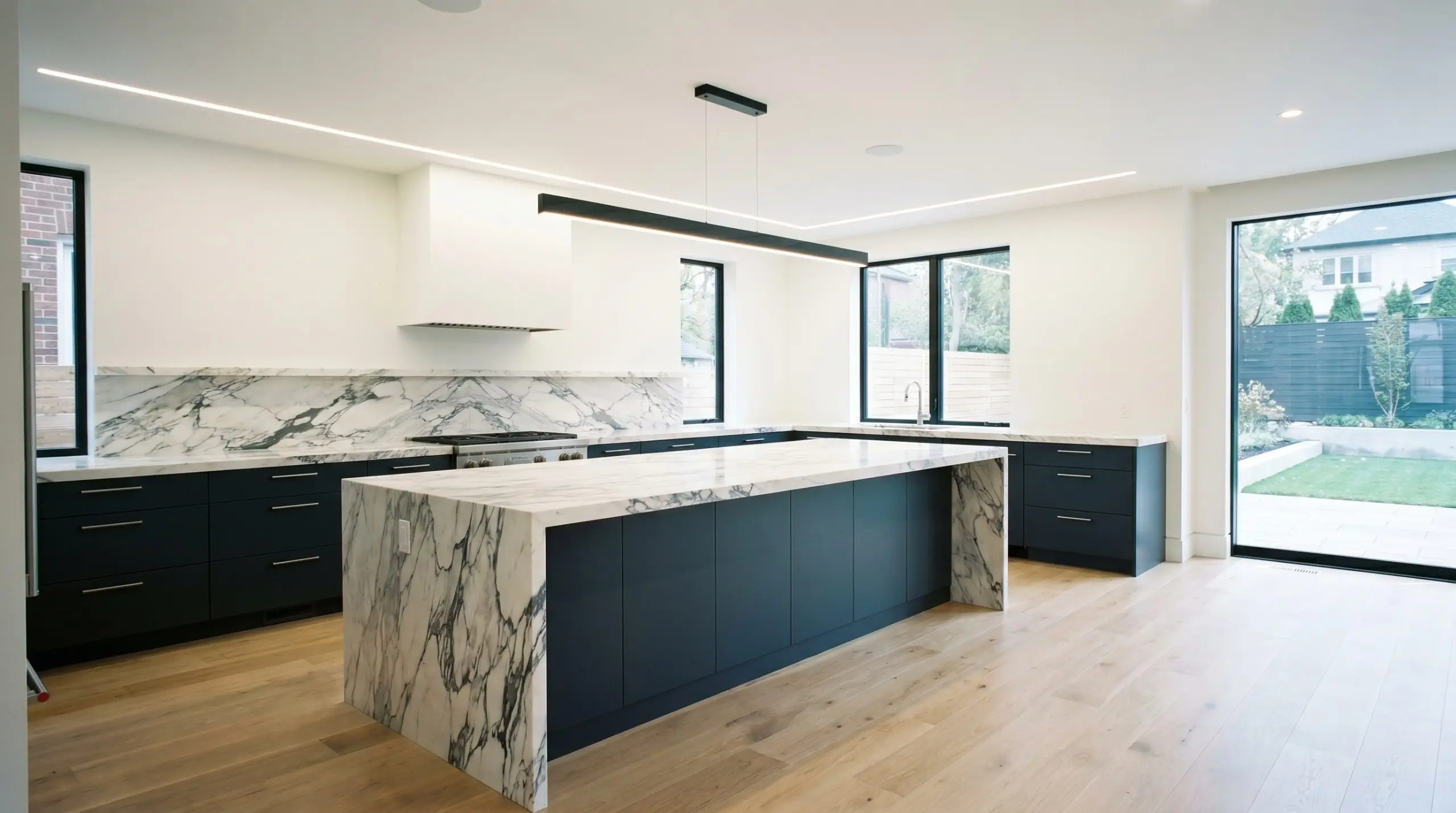 A sleek transitional kitchen features a massive central island and base cabinets painted in Benjamin Moore Polo Blue (Hex #333b44) topped with heavily veined calacatta viola marble.