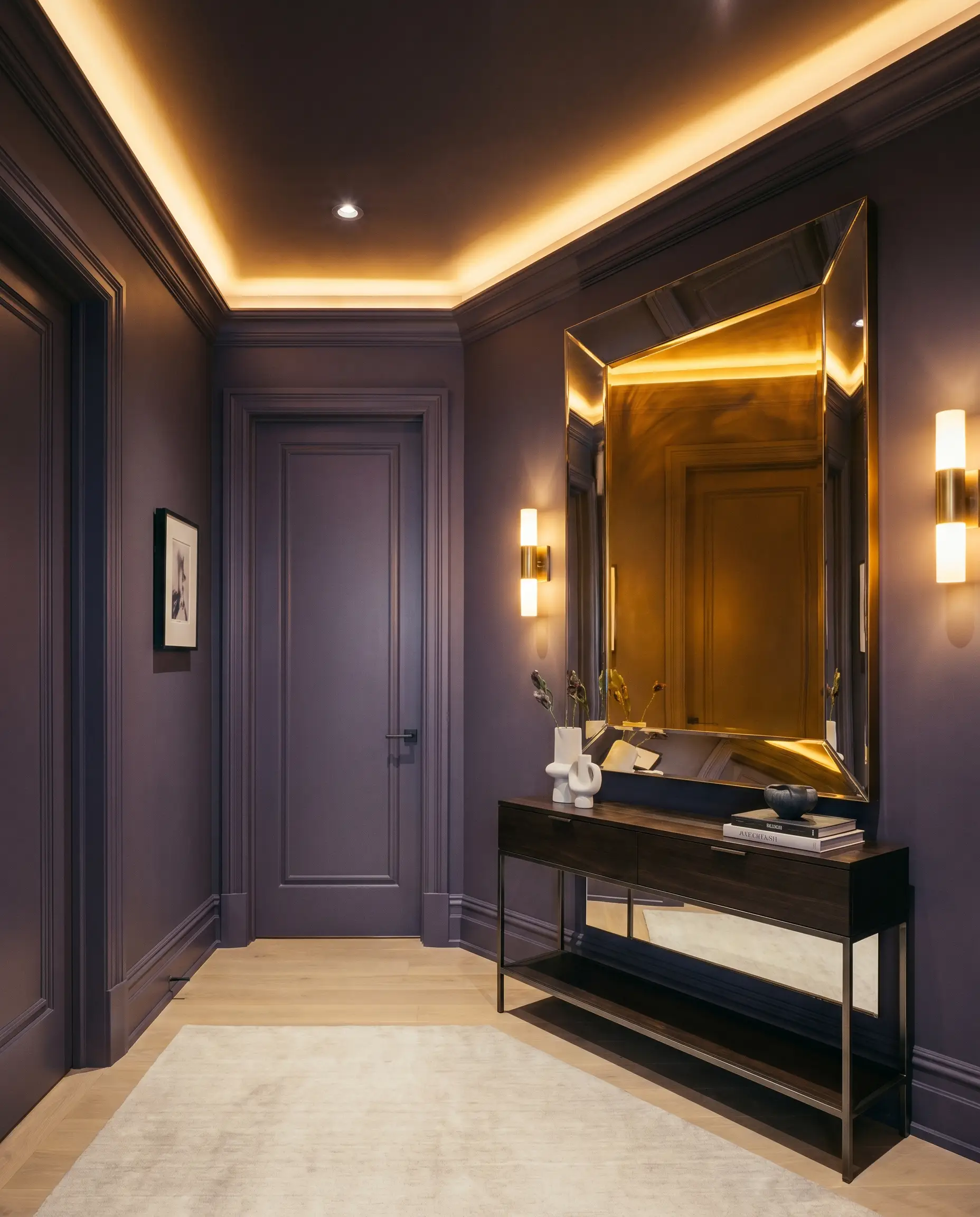 A sleek modern console table and oversized reflective mirror anchor a dramatic windowless entryway foyer color-drenched in Benjamin Moore Shadow (Hex #514A58).