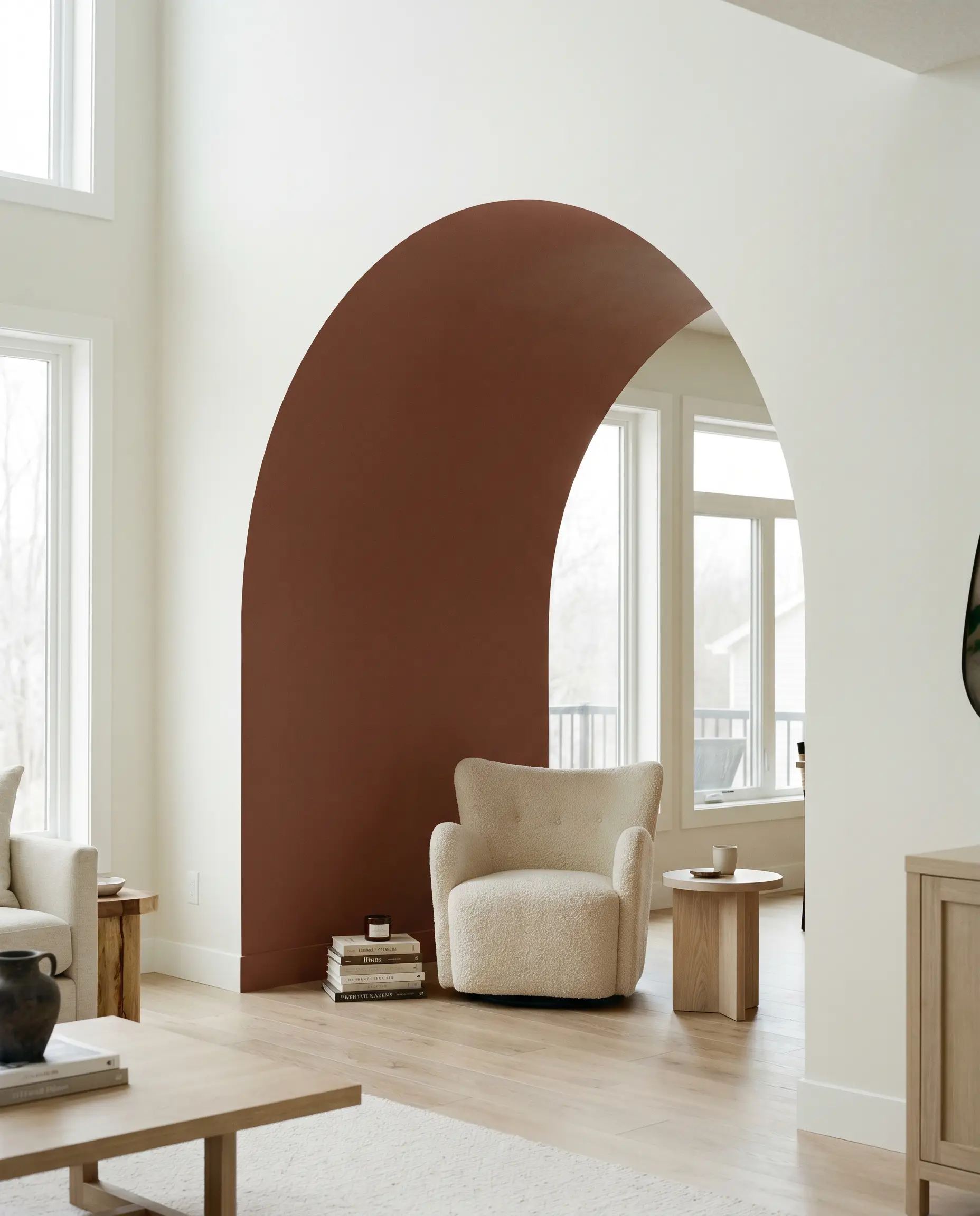 A large architectural archway painted in a warm brown-red tone frames a cozy reading nook featuring a textured bouclé chair and white oak side table.