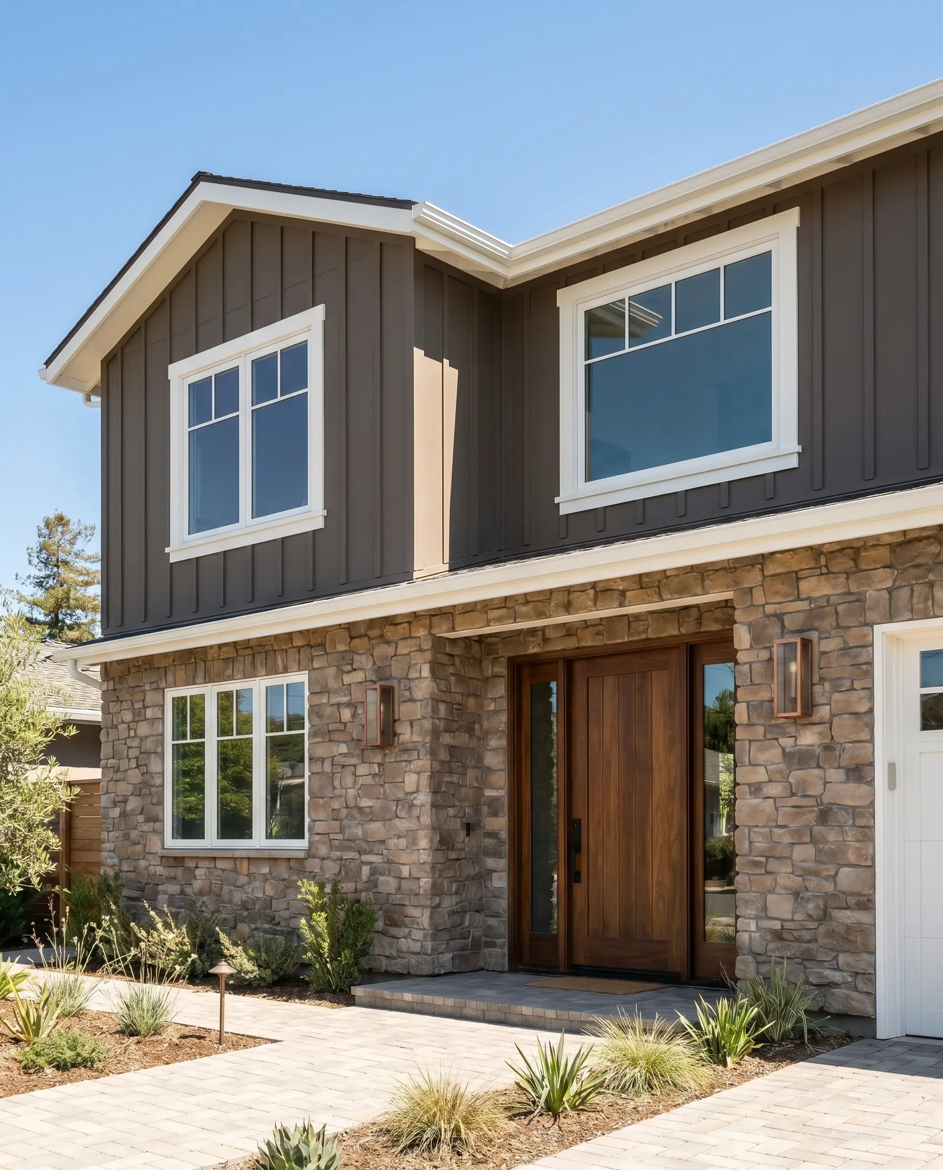 A two-story transitional home facade painted in Benjamin Moore Deep Creek (Hex #6B655B) features natural stone masonry, a warm walnut front door, and crisp trim.