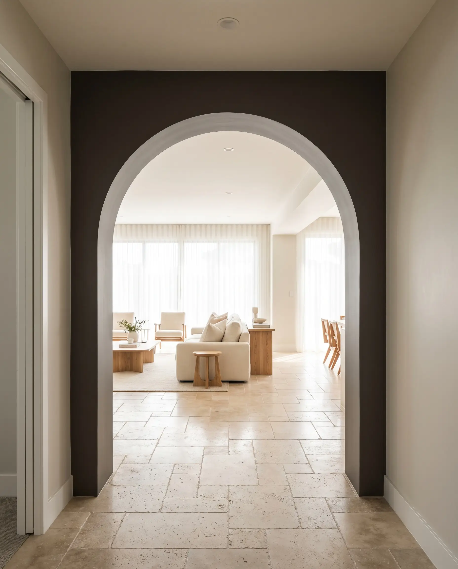 A thick architectural archway color-drenched in Benjamin Moore Night Horizon frames a bright living room featuring tumbled travertine stone floors.