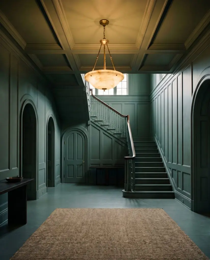 A vintage alabaster pendant light pierces the ceiling of a grand foyer where baseboards, walls, and interior doors are entirely color-drenched in a cool green.