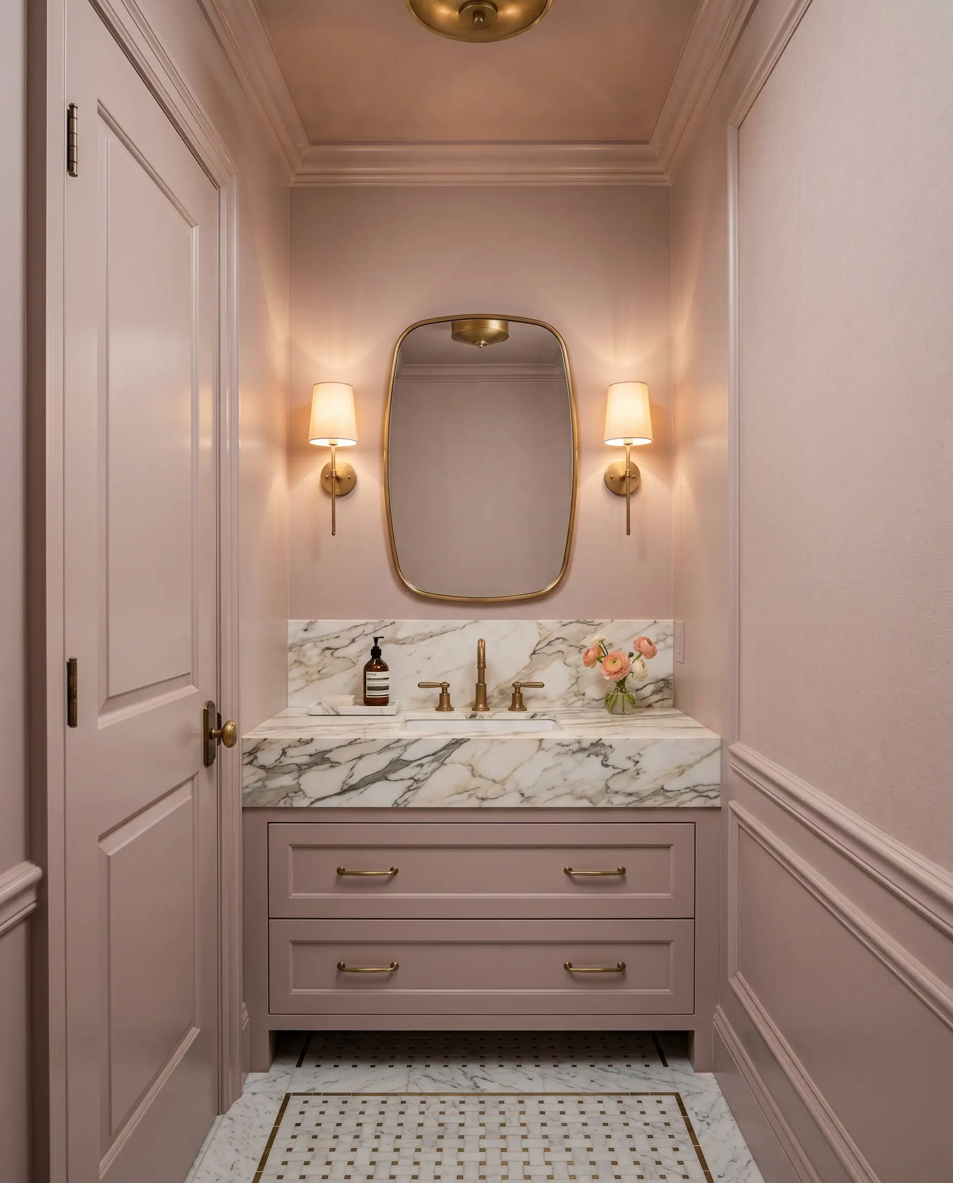 Shaded sconces illuminate a color-drenched warm blush powder bathroom featuring a heavily veined marble vanity top and an unlacquered brass faucet.