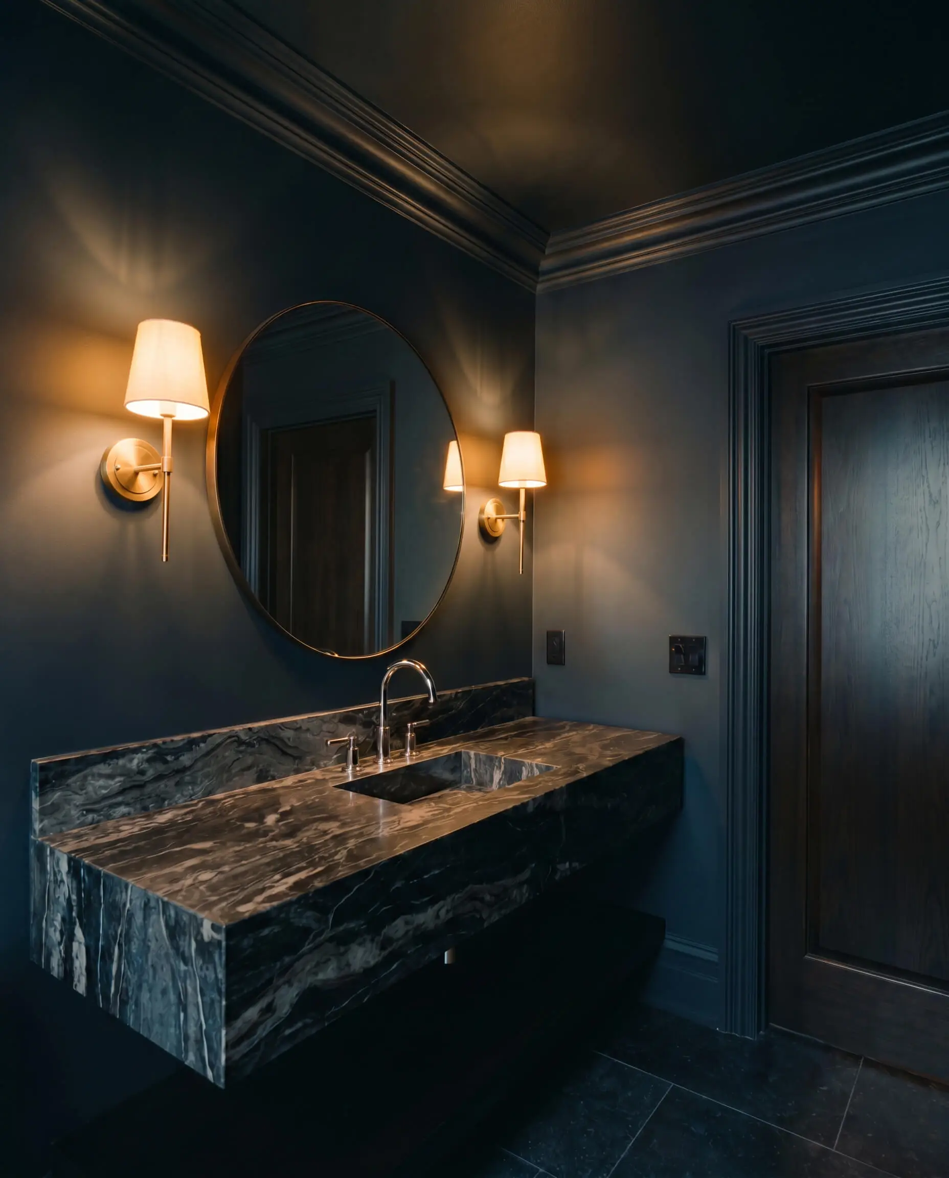A heavily veined marble vanity and polished nickel fixtures anchor a moody powder room enveloped in velvety blue-black paint.