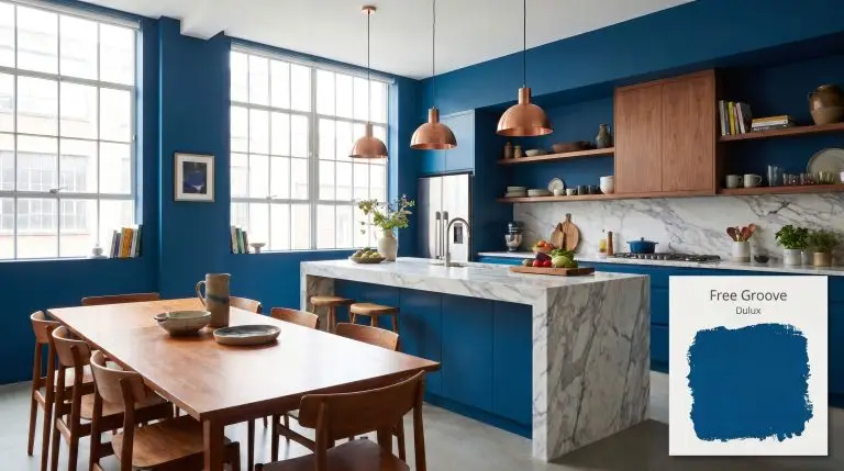 A modern transitional open-plan kitchen features lower cabinets and walls painted in Dulux Free Groove (Hex #024A7F), a marble island, and brushed copper pendants.