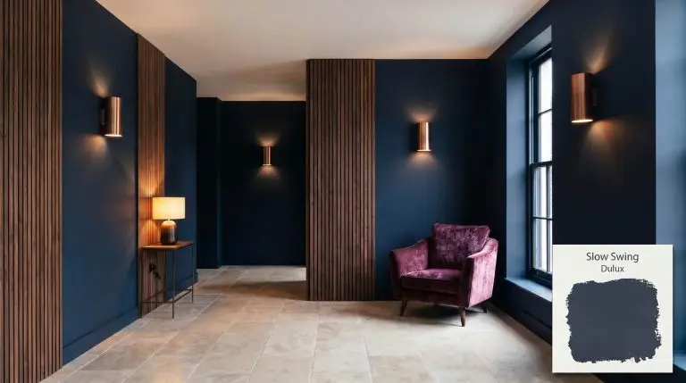 Fluted walnut wood paneling and a crushed velvet accent chair define this sophisticated modern lounge painted in Dulux Slow Swing (Hex #2C3241).