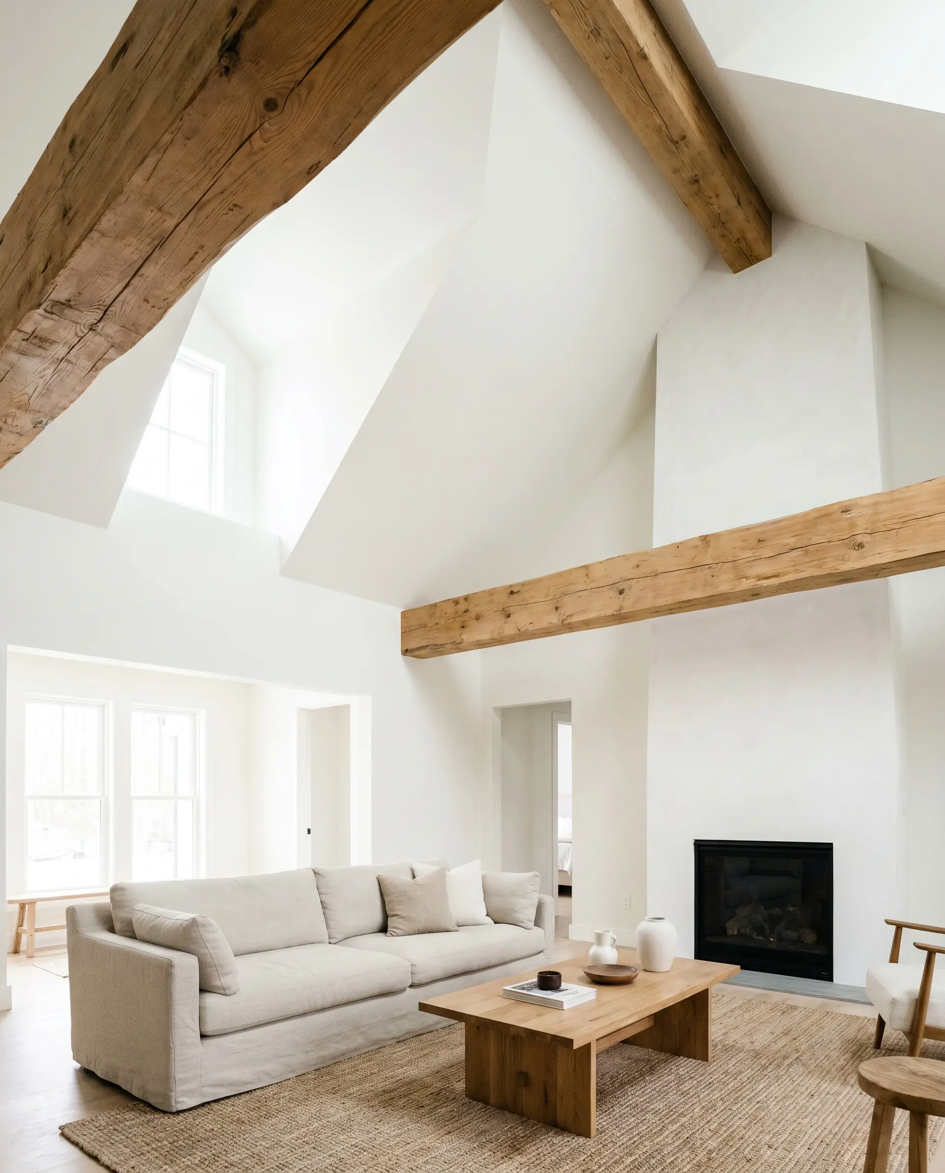 Exposed natural wood beams span a soaring cathedral ceiling and walls painted in PPG Delicate White (Hex #f1f2ee), creating massive ambient light absorption in the living space.