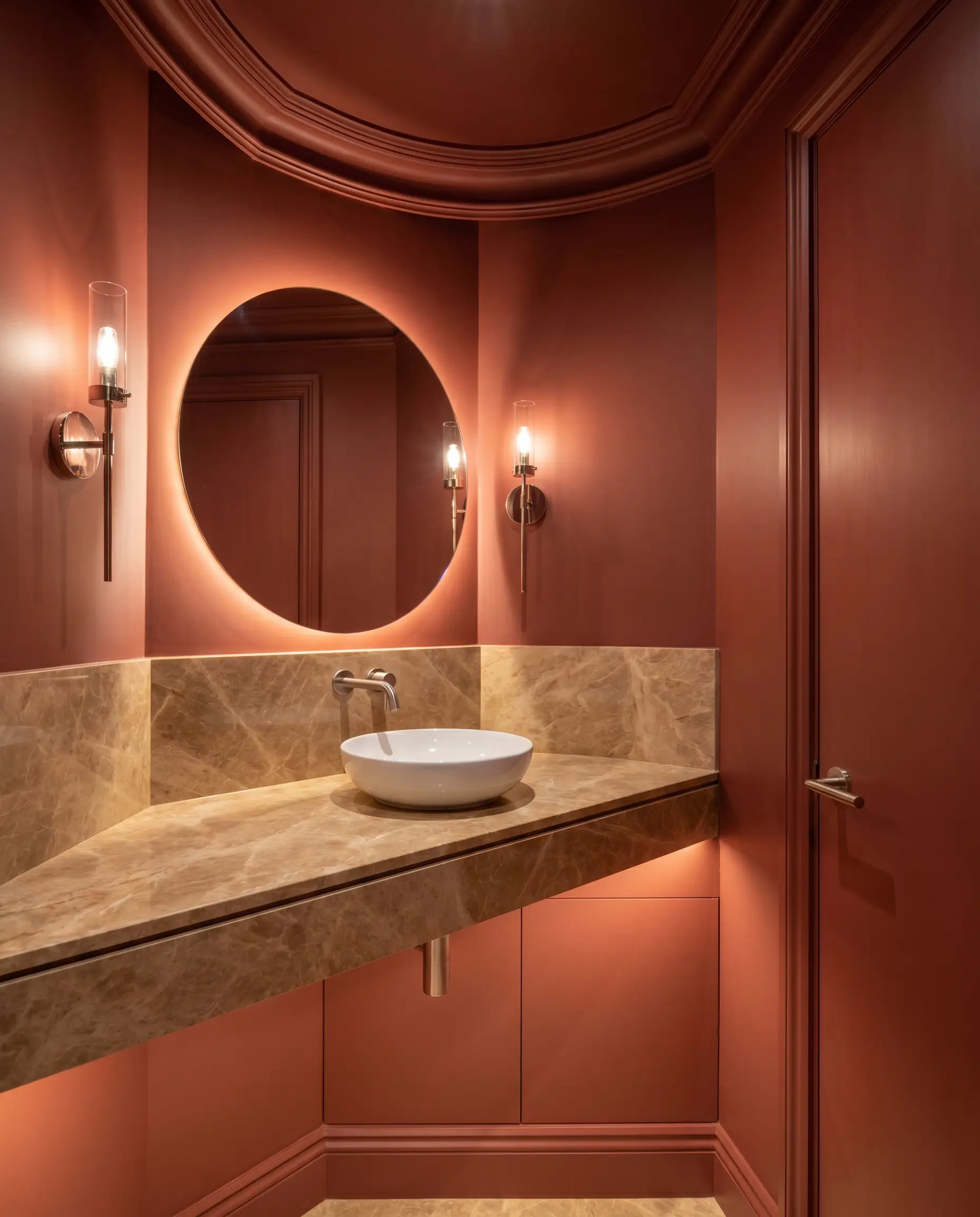A windowless guest powder room features complete color drenching in Farrow & Ball Picture Gallery Red (Hex #9b594f) across the walls, trim, ceiling, and door, contrasting with a floating warm-veined marble vanity and polished nickel sconces.