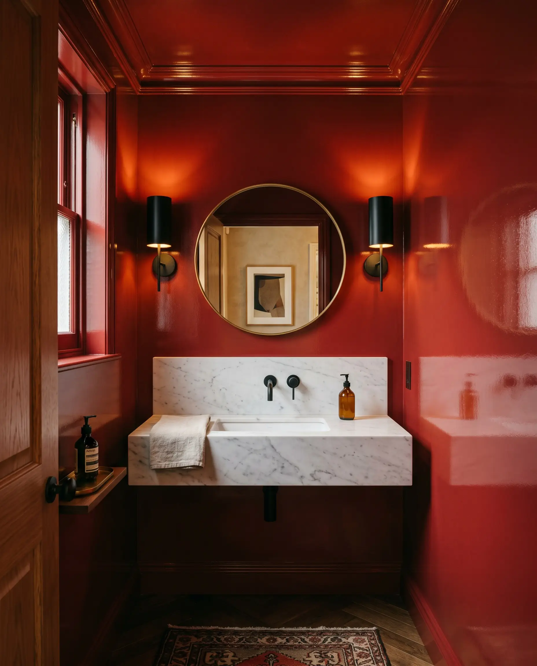 A jewel-box powder bath painted in high-gloss Benjamin Moore Red features a floating honed marble sink, matte black steel sconces, and a minimalist brass mirror.