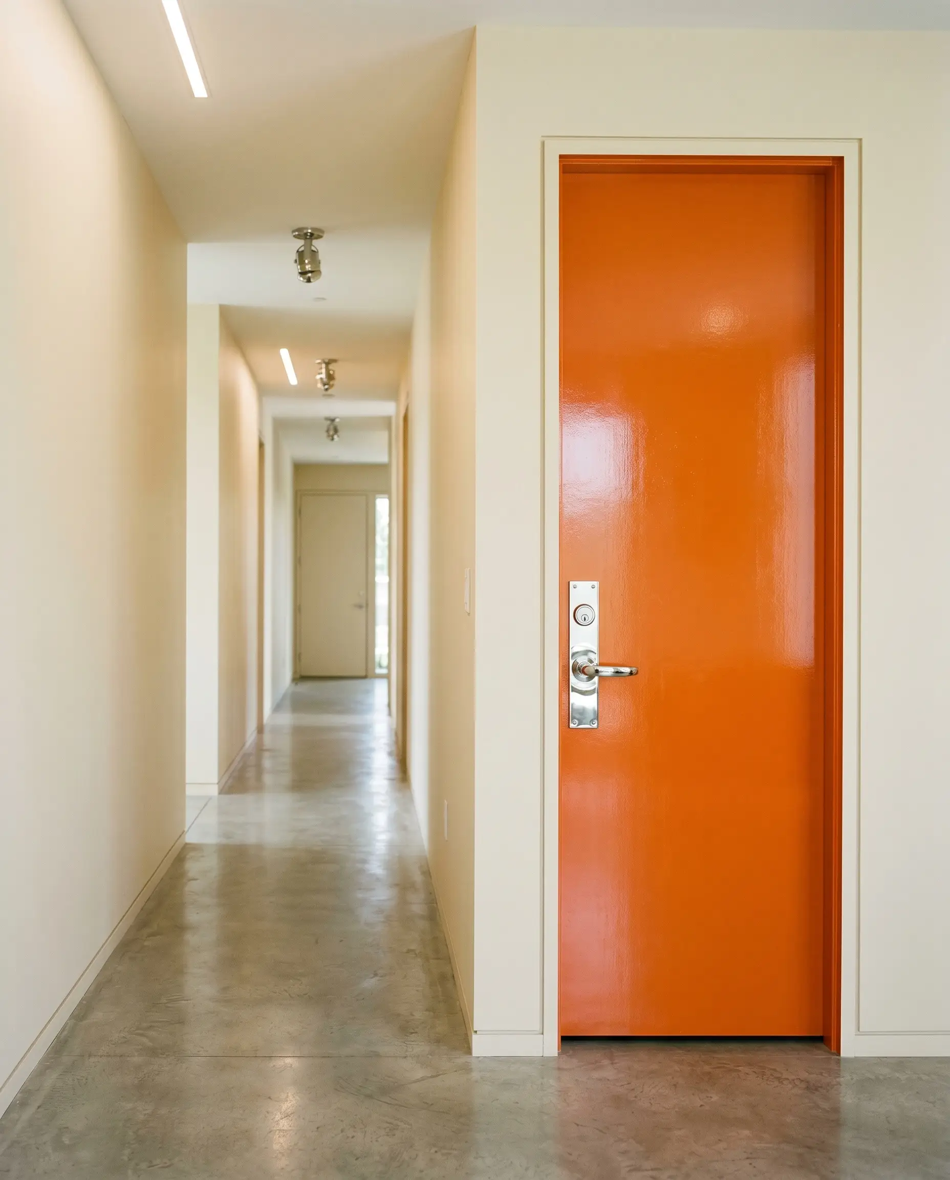 A standard door painted in a high-gloss finish of Benjamin Moore Electric Orange (Hex #F0701A) stands out against flat warm cream hallway walls.