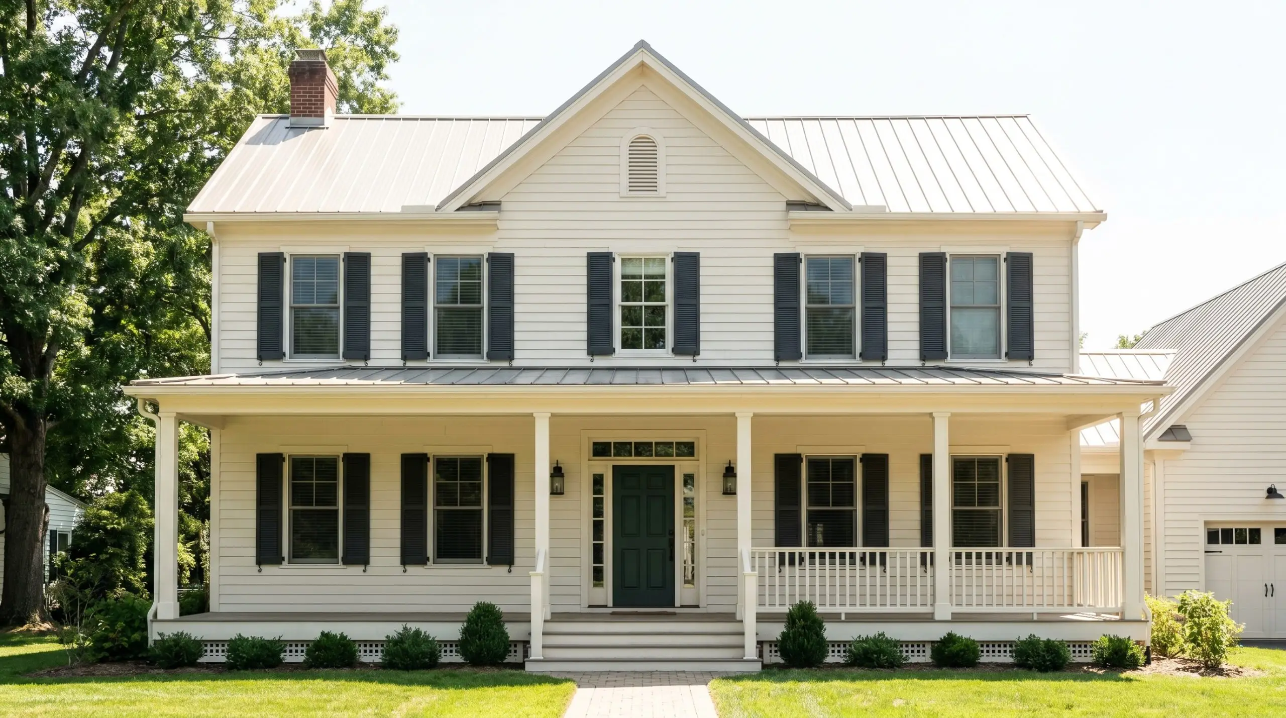 Dark charcoal shutters and a deep forest green front door punctuate the warm off-white exterior siding of a classic historic home facade.