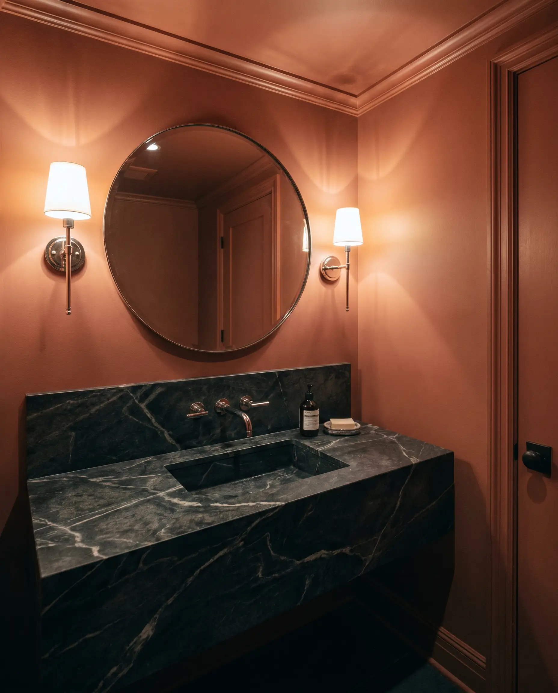 A moody traditional windowless powder room features walls and ceiling seamlessly painted in Benjamin Moore Baked Terra Cotta (Hex #B36957) alongside a dark soapstone vanity.