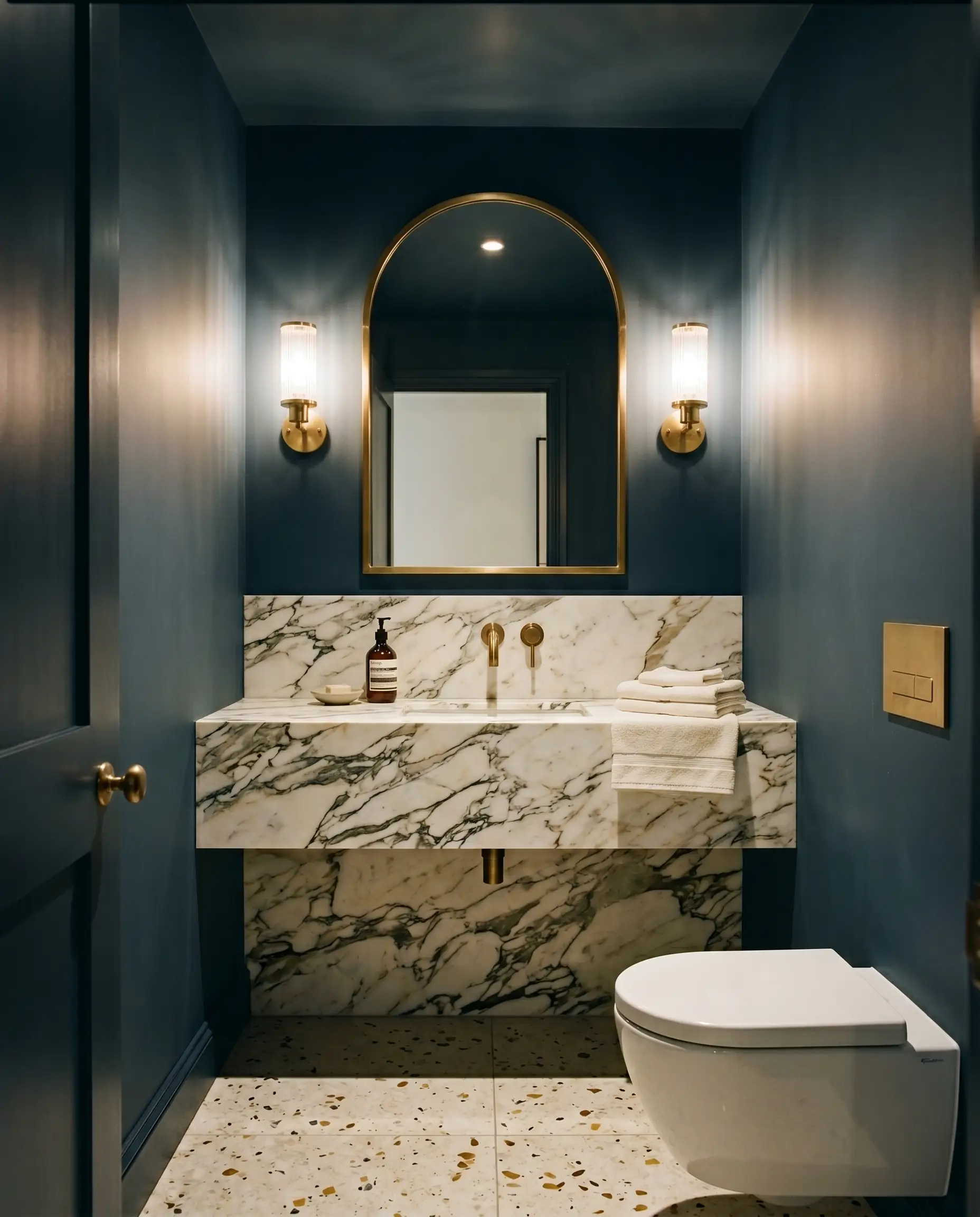 A heavily veined Calacatta marble vanity and unlacquered brass fixtures stand against walls and ceiling painted in Farrow & Ball Hague Blue (Hex #3f4d57).