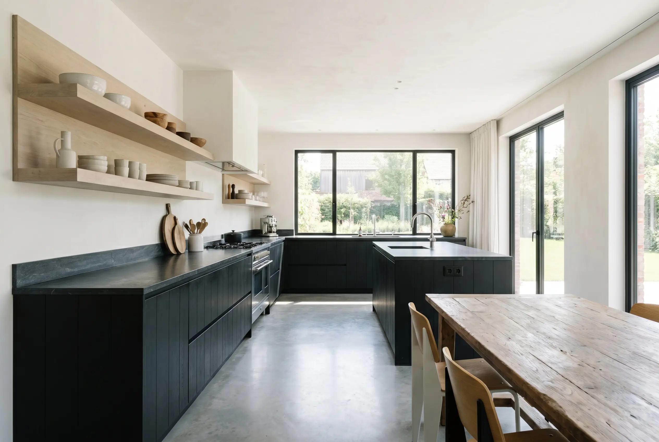 Sophisticated lower kitchen cabinetry painted in a warm soft black contrasts sharply against pale bleached oak open shelving and honed soapstone countertops.