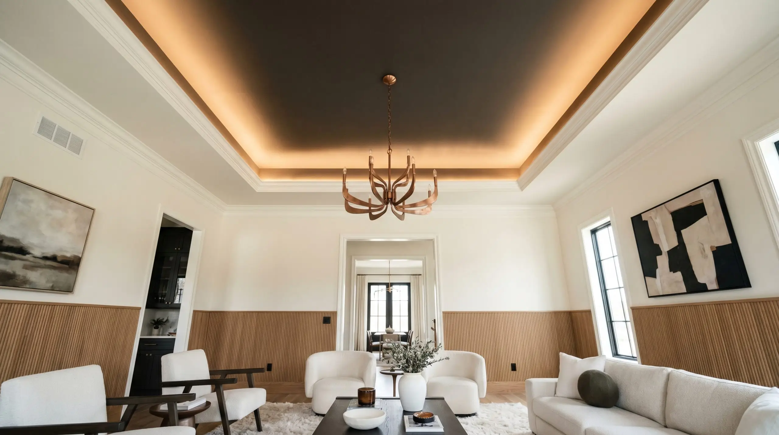 A modern brushed copper chandelier hangs below a dark caffeinated brown recessed tray ceiling framed by light walls and fluted oak wall accents.
