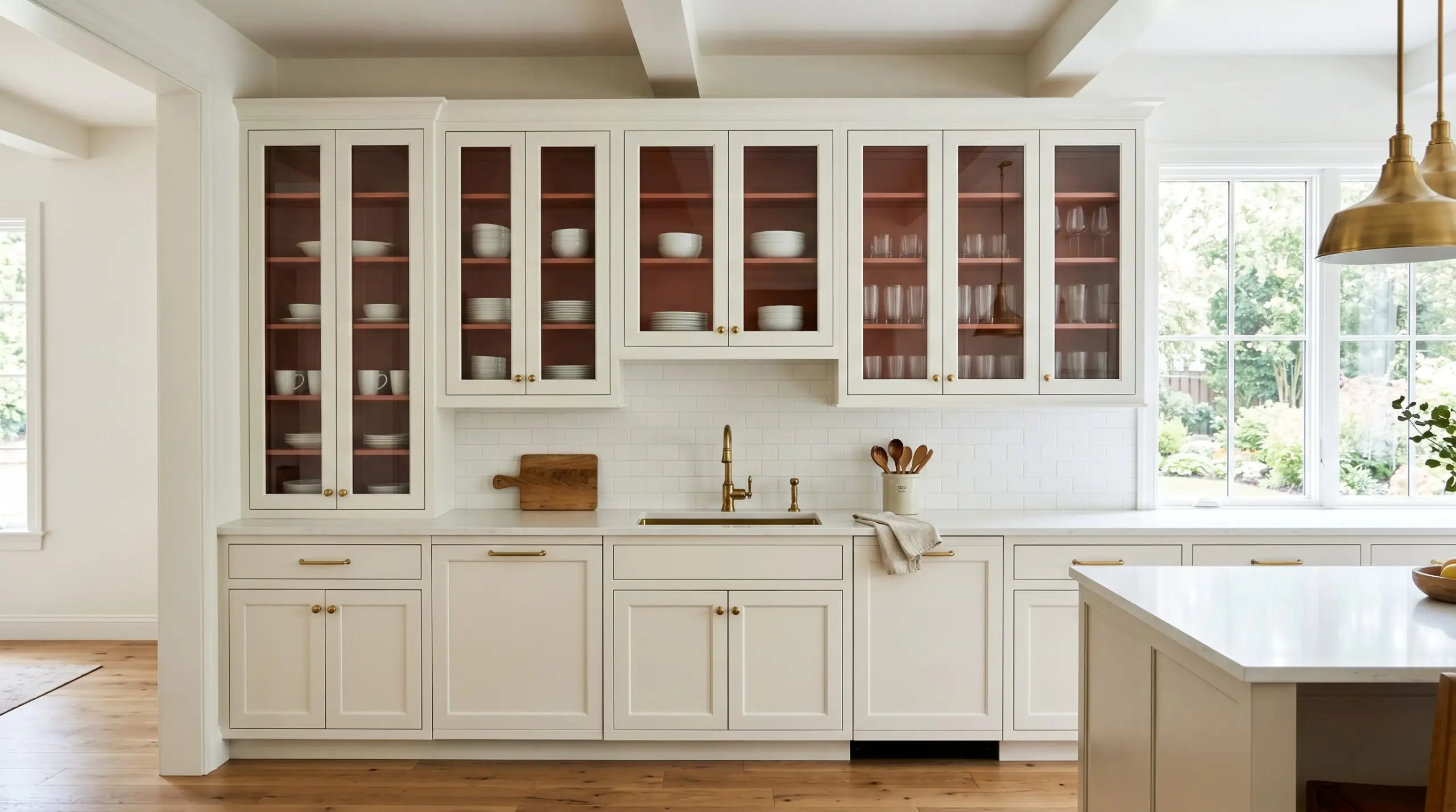 Crisp white dishware and clear reeded glass display beautifully behind unlacquered brass hardware against a muted warmth interior cabinet backing in a transitional kitchen.