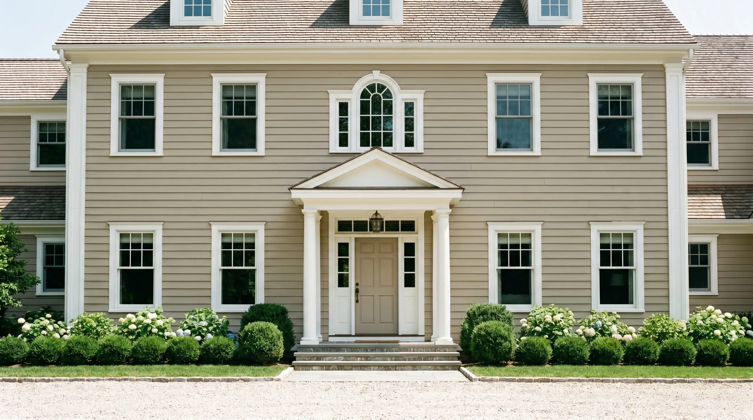 A classic colonial exterior facade features earthy khaki traditional siding paired with crisp white trim under bright midday sunlight.