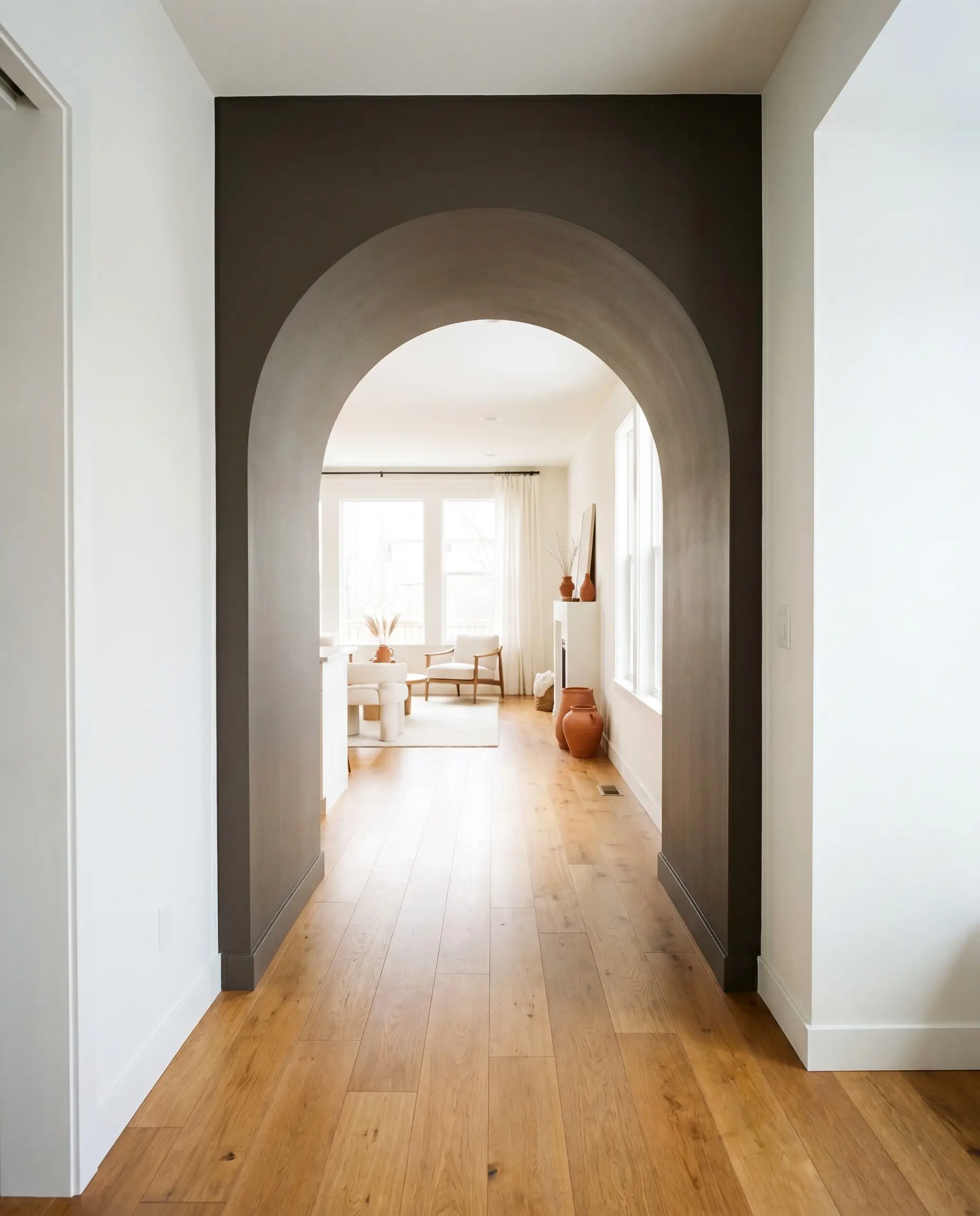 A deep earthy brown structural archway casing frames a transition hallway featuring warm honey oak flooring and clean white walls leading into a living room.