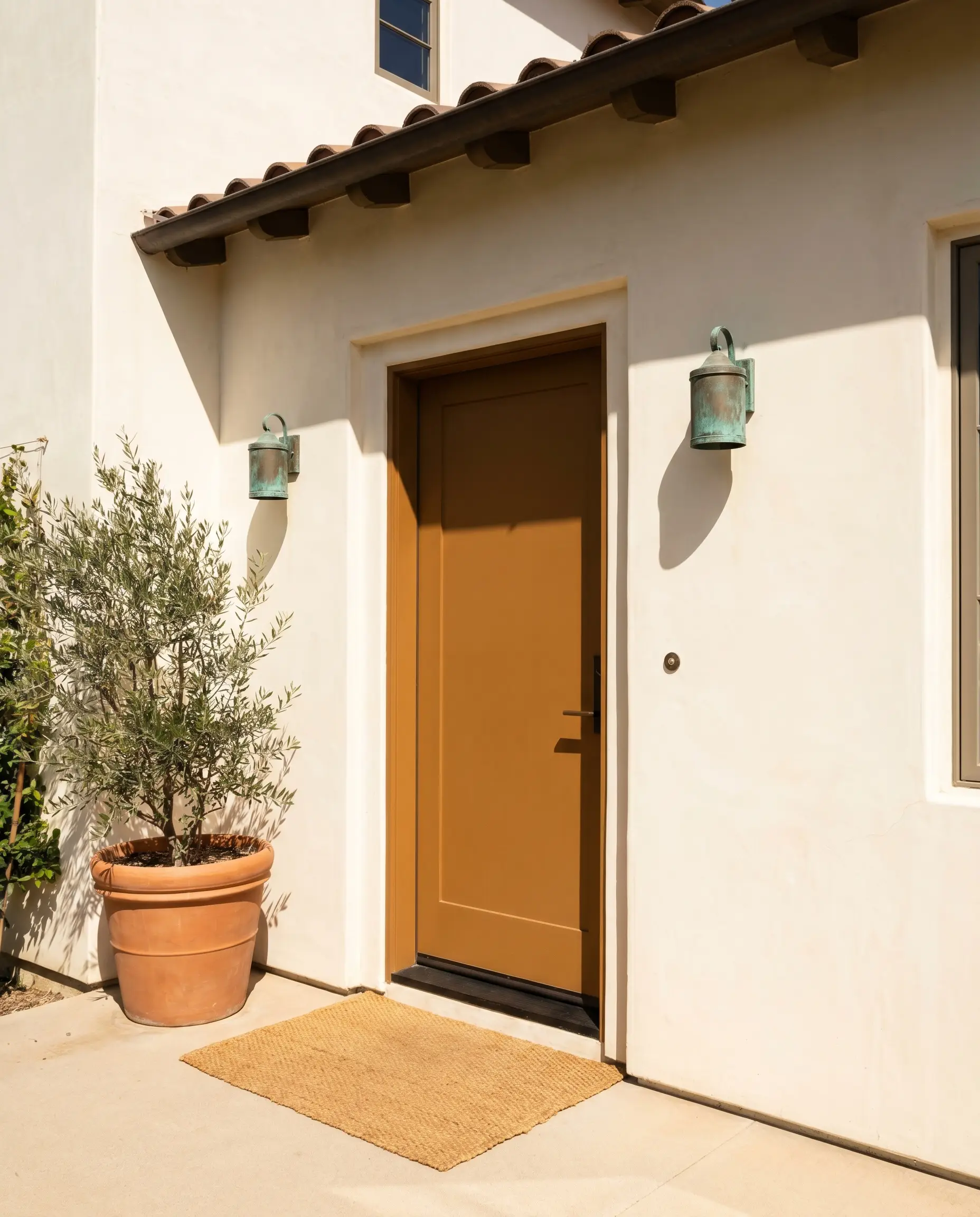 A front door painted in Dulux Tuscan Terracotta (Hex #D8967B) contrasts beautifully with a creamy off-white stucco facade and aged copper exterior sconces.