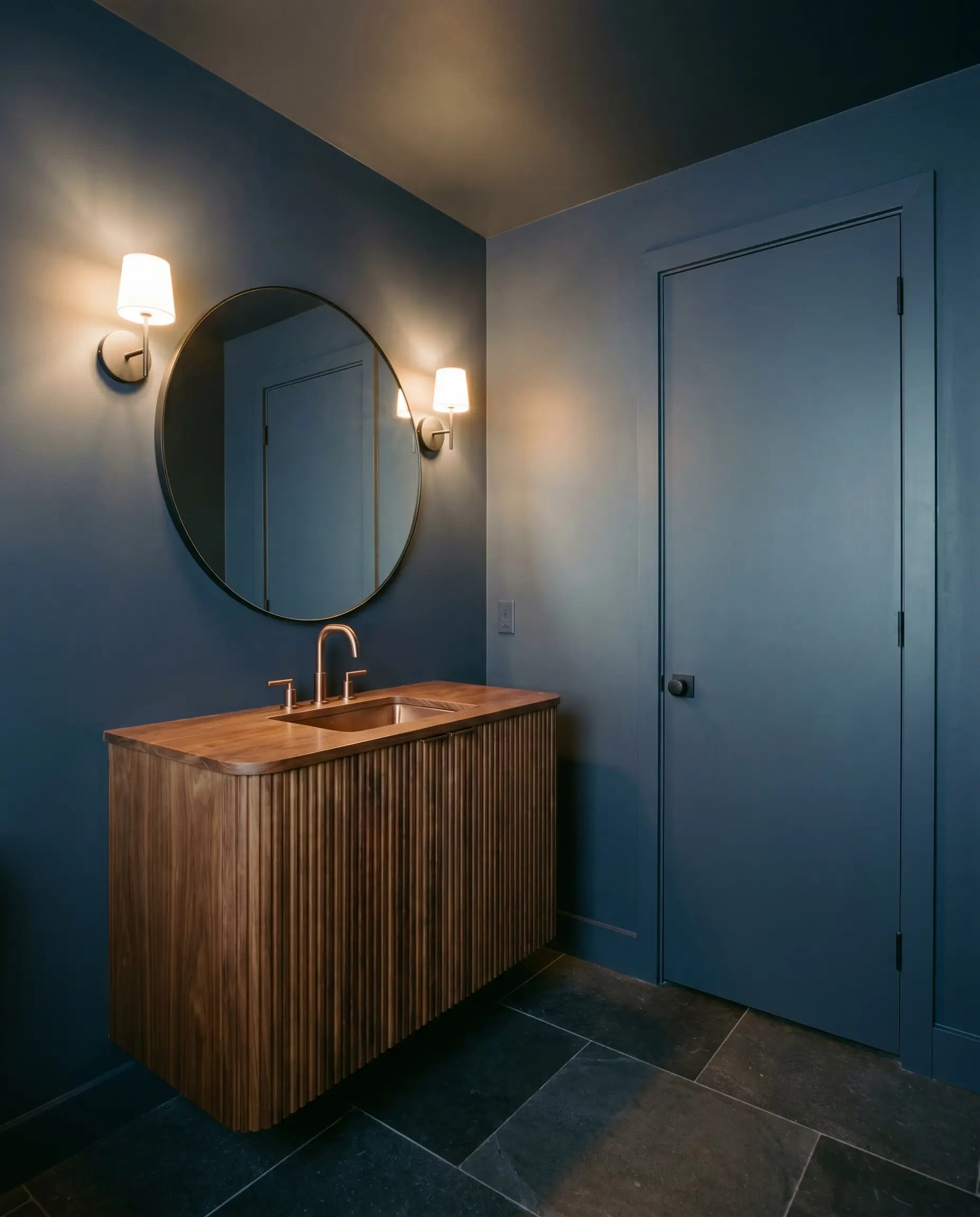 A fluted walnut vanity and brushed copper faucet stand out in a moody, jewel-box powder room wrapped entirely in deep indigo-blue.