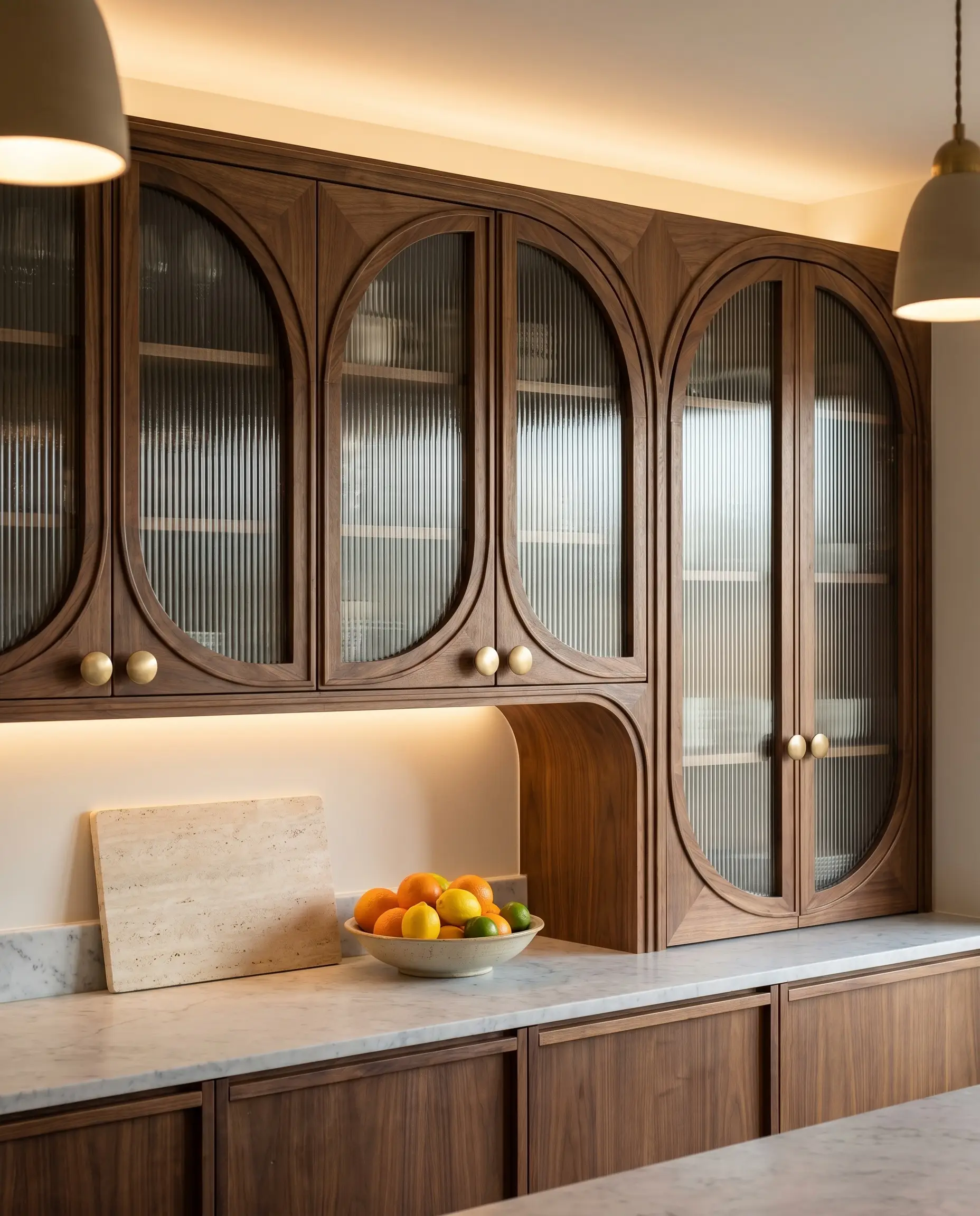 Steam-bent solid walnut arched frames encase fluted glass upper cabinets mounted above a pristine marble countertop and flat-panel wood bases.