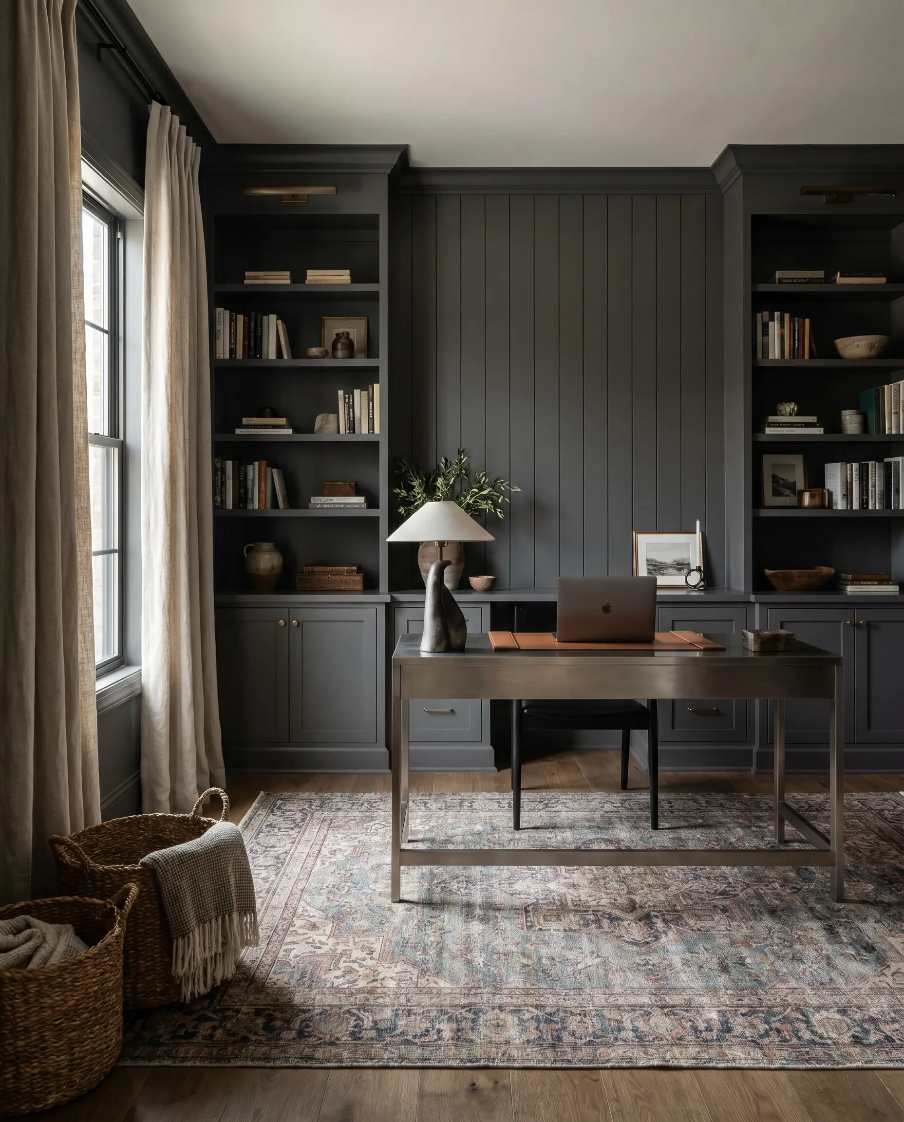 Custom built-in bookcases and a slatted wood accent wall painted in Benjamin Moore Gray frame a sleek metal console desk and faded vintage rug.