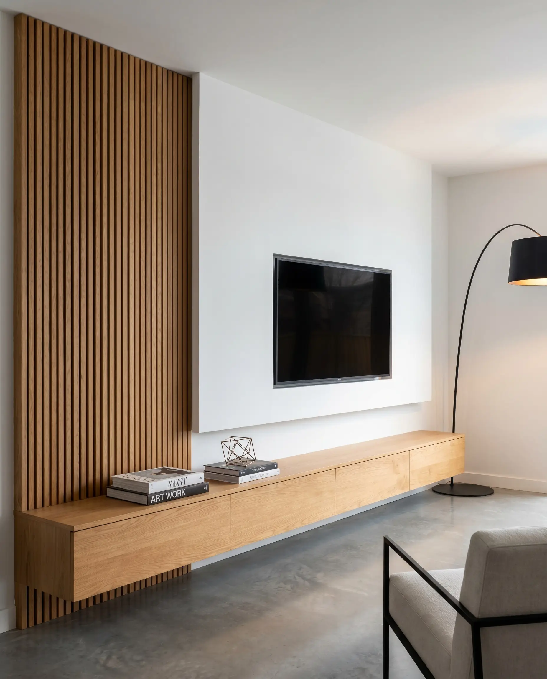 An off-center mass of acoustic wood slat panels contrasts against flat white drywall beside a mounted television, oversized black floor lamp, and floating oak console.