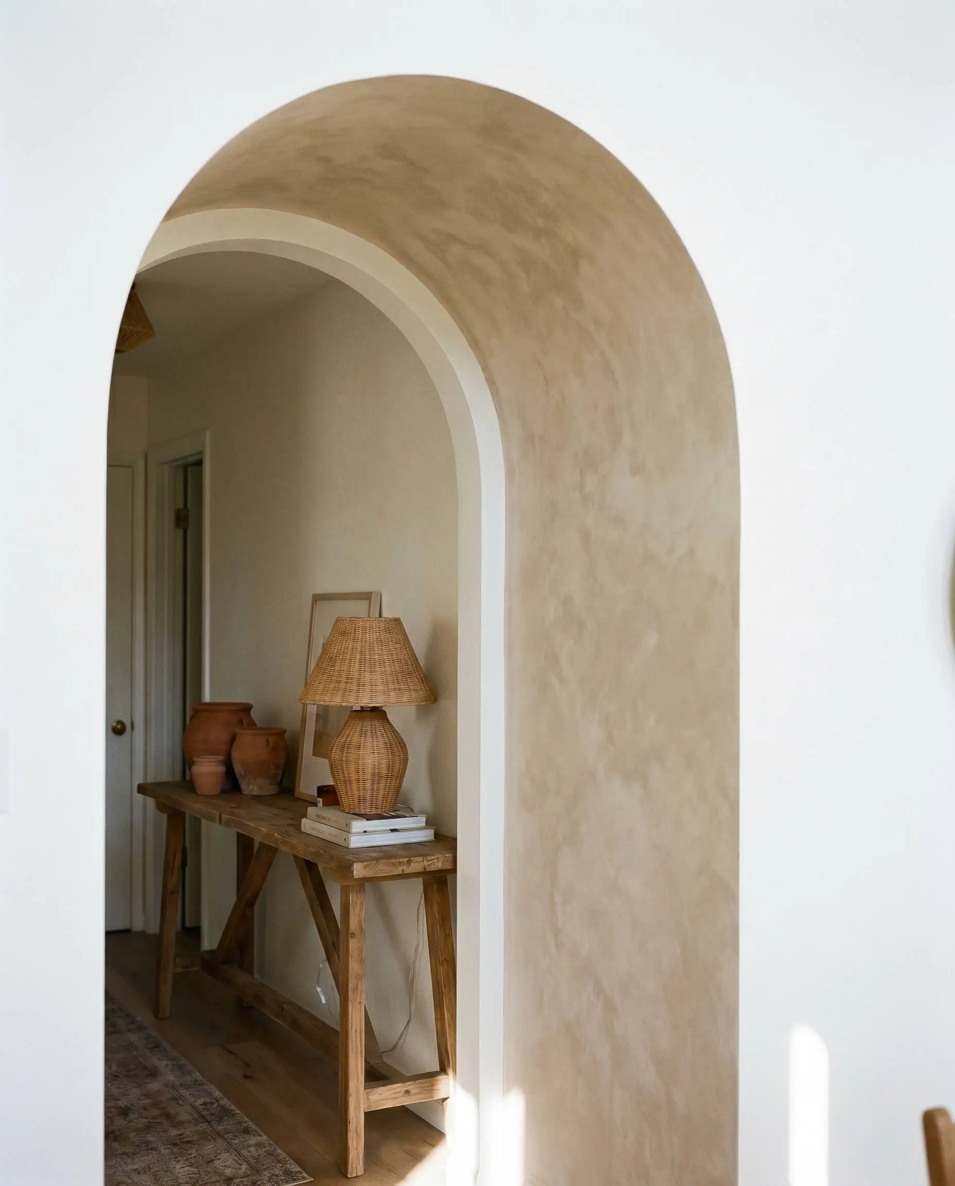 A soft beige limewash finish coats the inside curve of an arched doorway, contrasting sharply against the stark white flat drywall of the surrounding space.