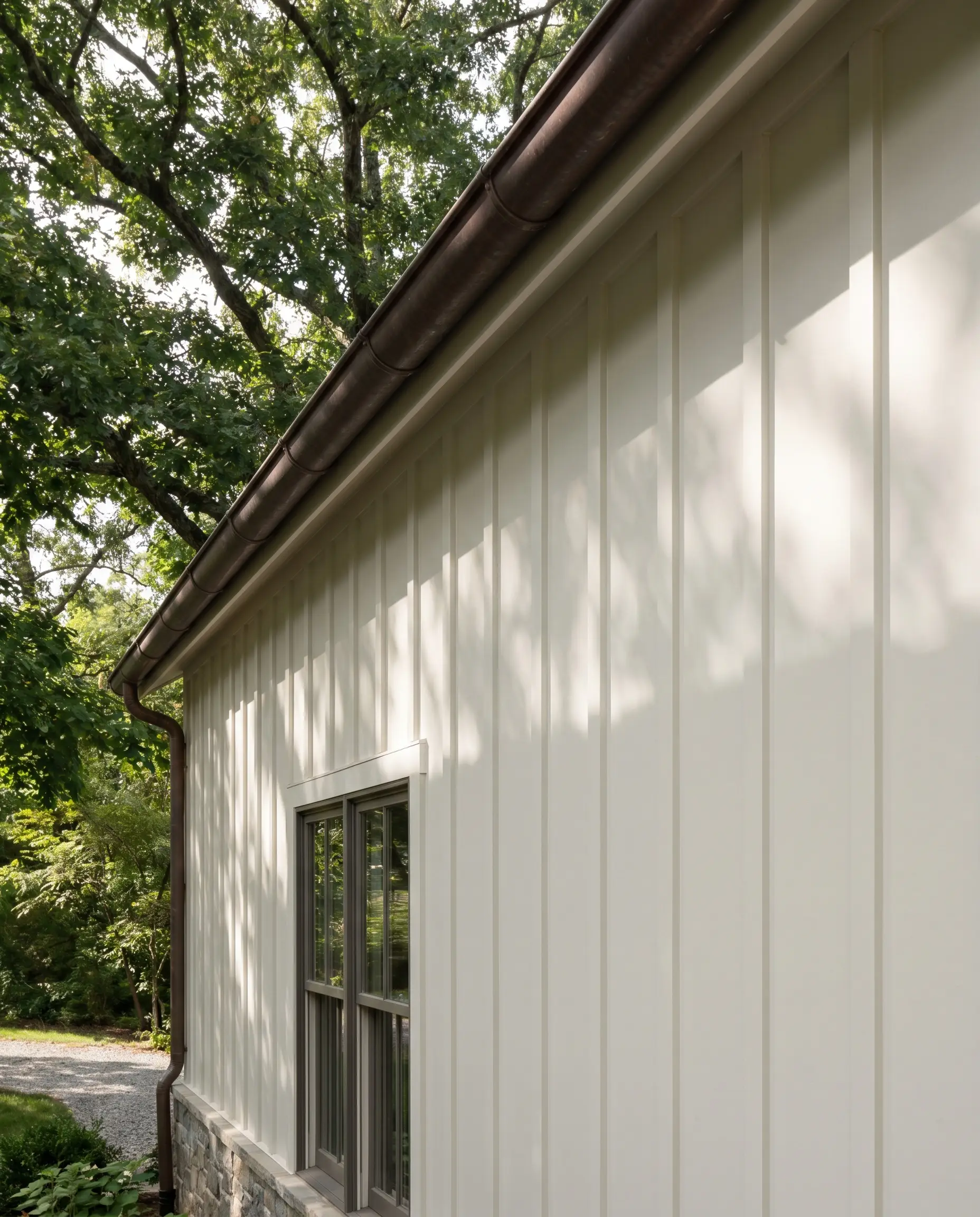 Crisp White Dove board and batten siding integrates with a traditional copper rain gutter and mature green foliage along the architectural roofline.