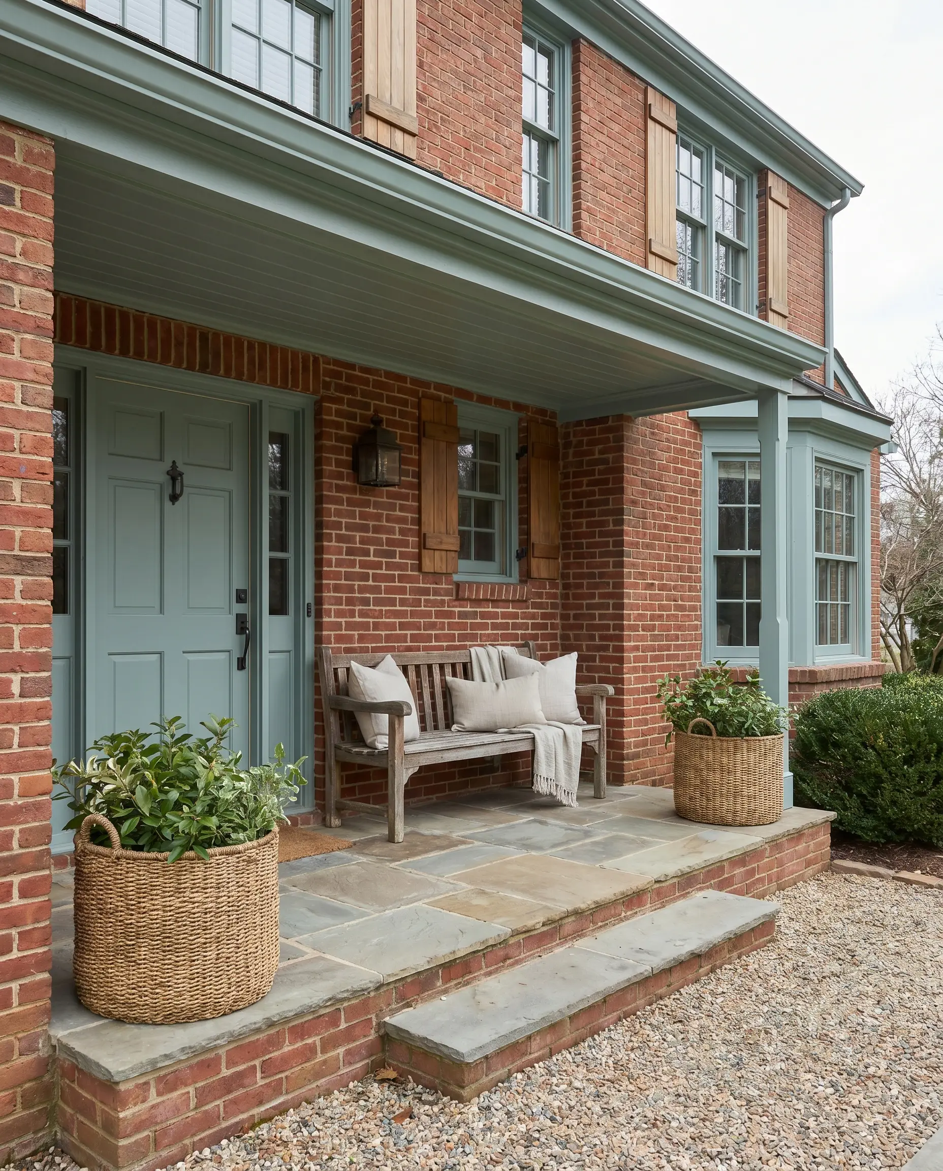 The best exterior colors for red brick houses include a muted blue-green painted front door and matching porch ceiling paired with woven outdoor planters.