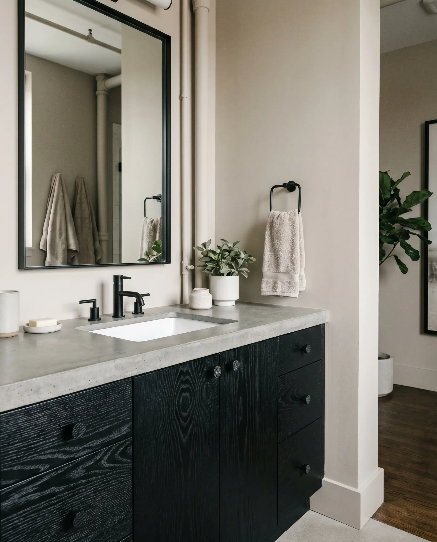 A heavily textured ebonized black ash vanity with knurled matte black hardware and a white under-mount sink stands against warm greige drywall.