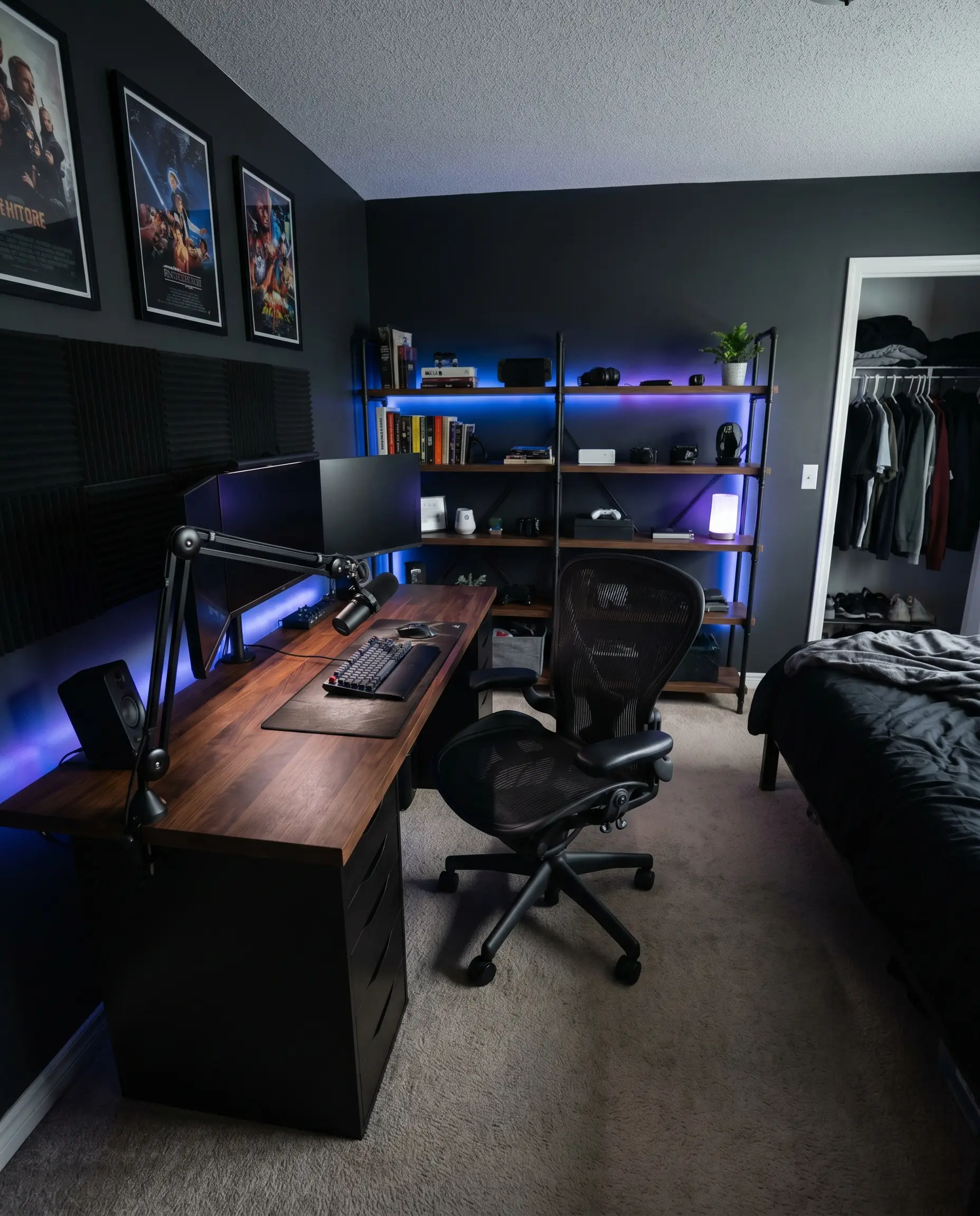 A sleek black mesh ergonomic task chair sits tucked under a modern wooden gaming desk against dark painted walls.