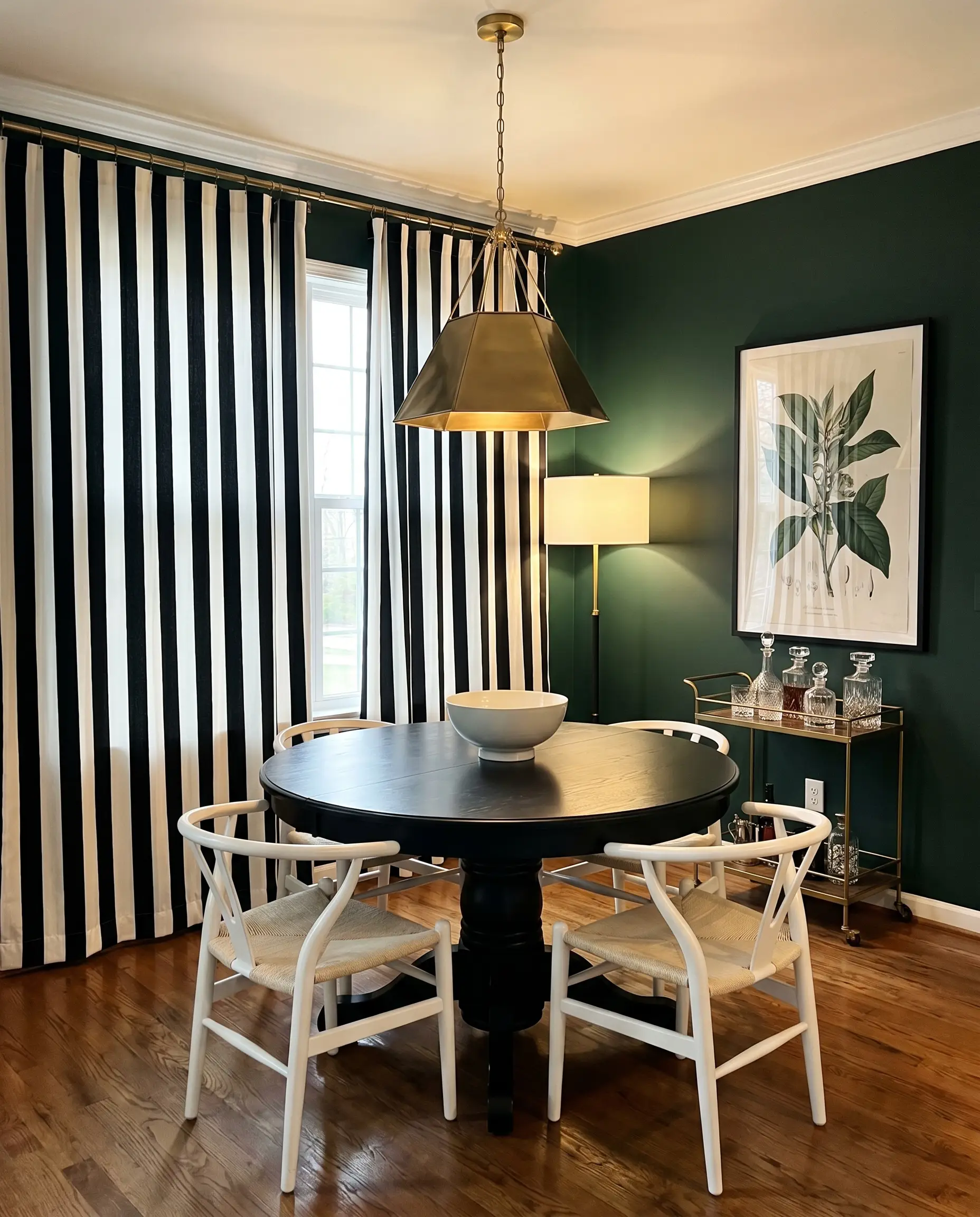 Bold black and white cabana stripe cotton canvas curtains frame a round black dining table surrounded by white wishbone chairs.