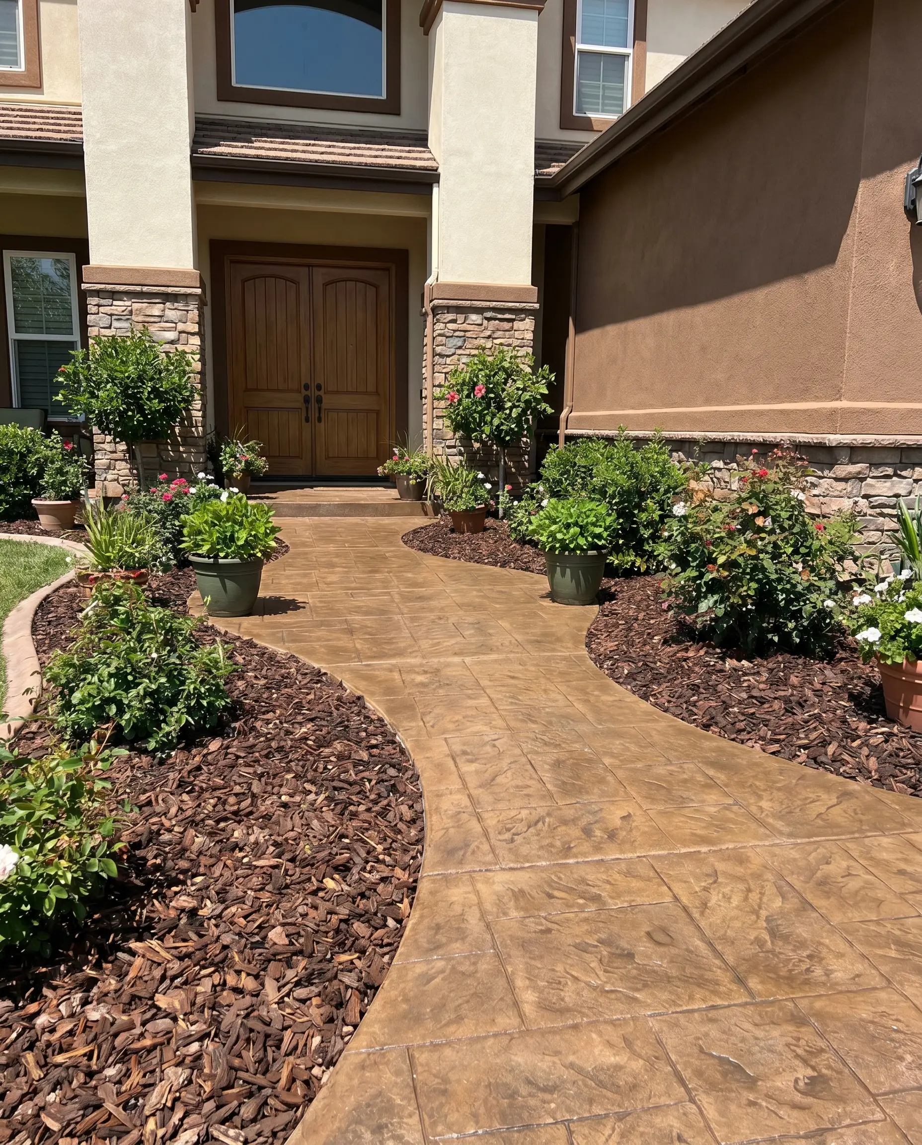 Bronze-toned concrete pavers form a front entry walkway bordered by landscaping beds filled with dark brown undyed hardwood bark mulch.