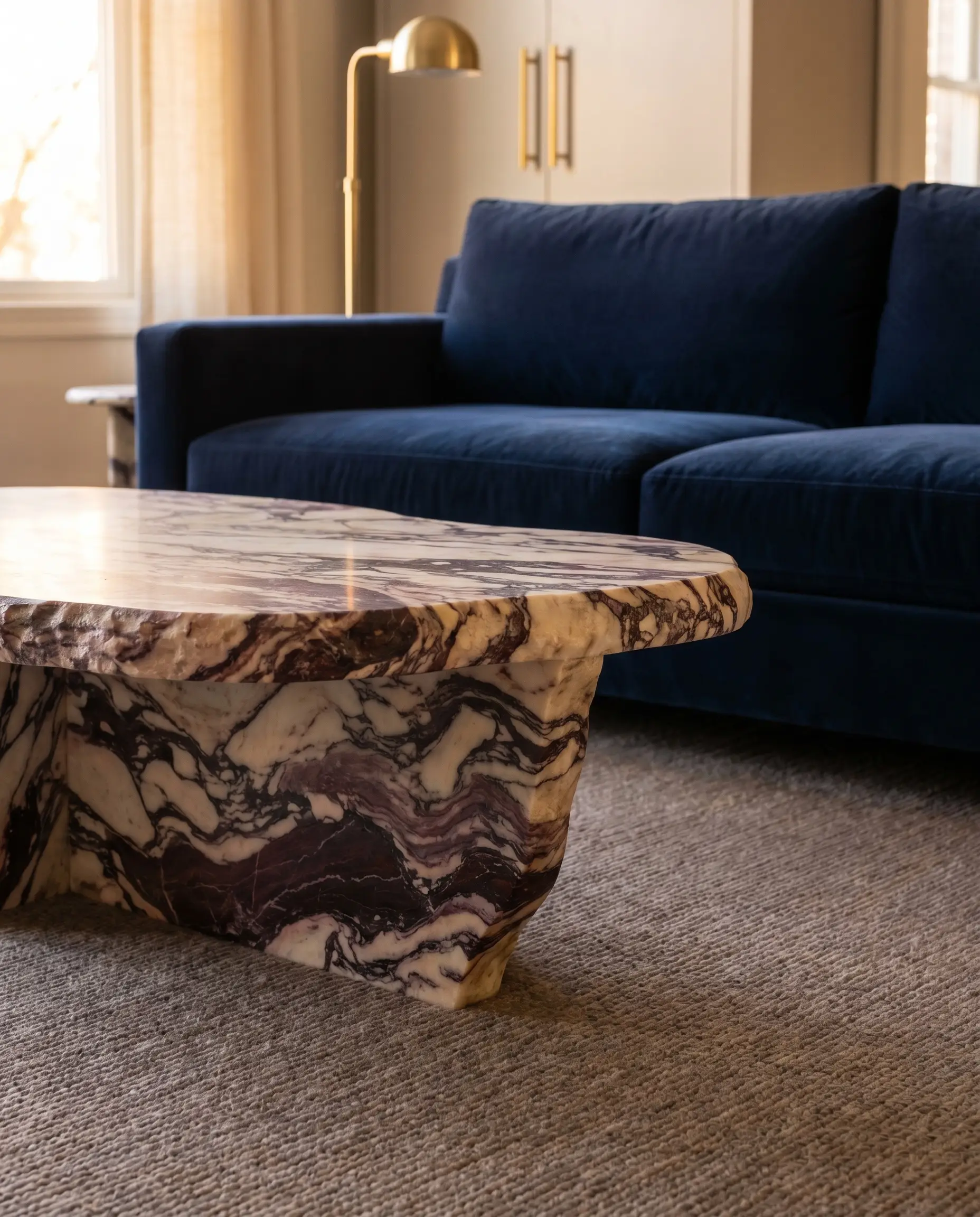 Heavily veined Calacatta Viola marble provides stunning coffee tables to match a navy blue sofa, featuring dramatic burgundy patterns above a muted rug.