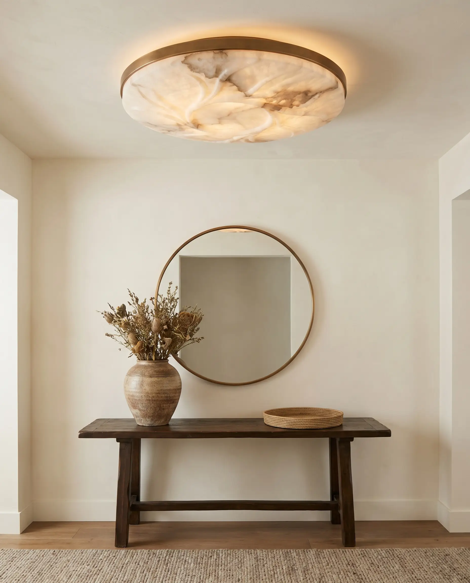 A carved natural alabaster flush mount with warm bronze detailing hugs a Benjamin Moore White Dove ceiling above an entryway console table and handcrafted ceramic vase.