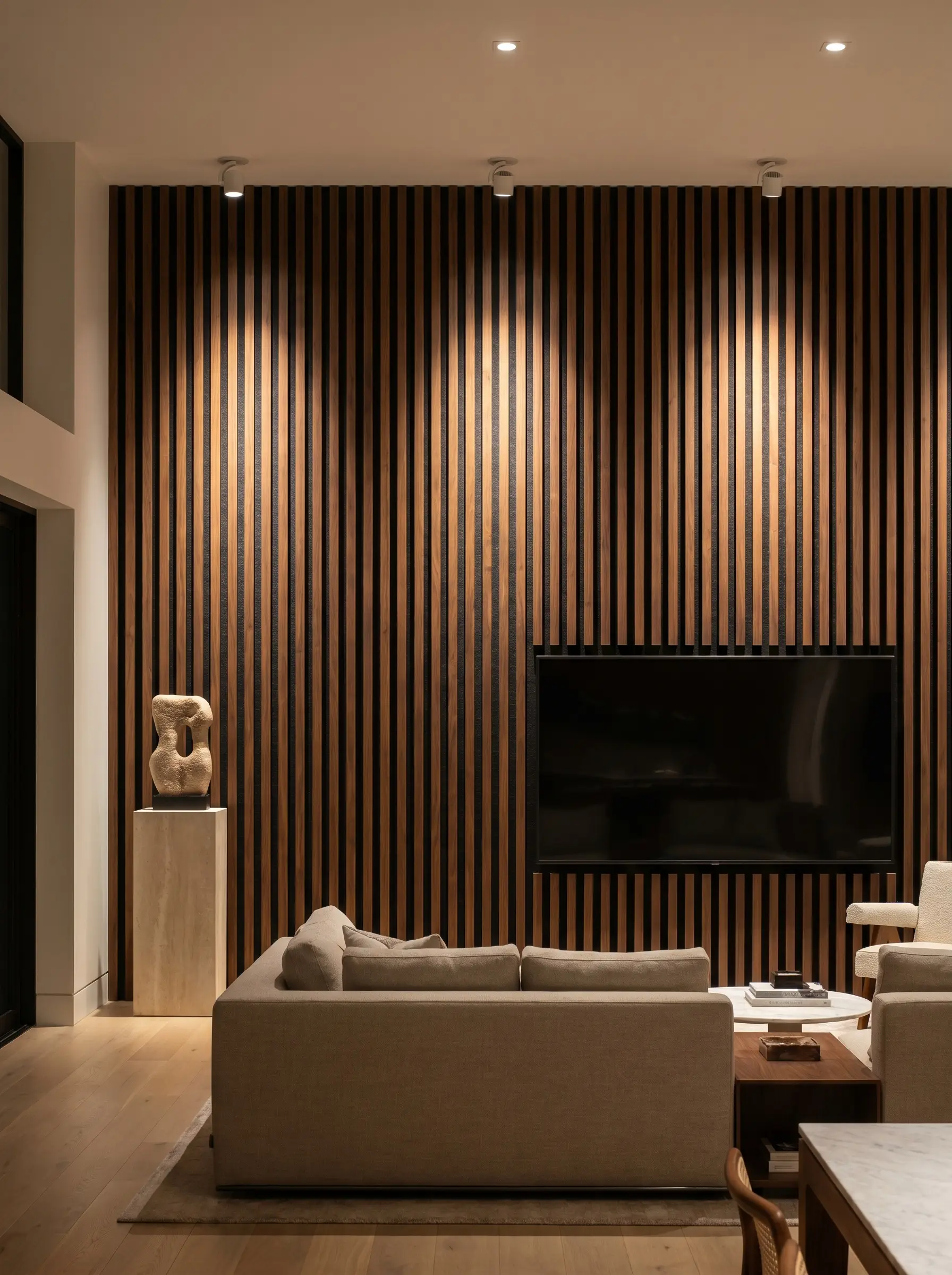 Adjustable ceiling-mounted gimbal spotlights cast dramatic shadows down a walnut wood slat media wall, highlighting the thick black acoustic felt grooves behind a television.