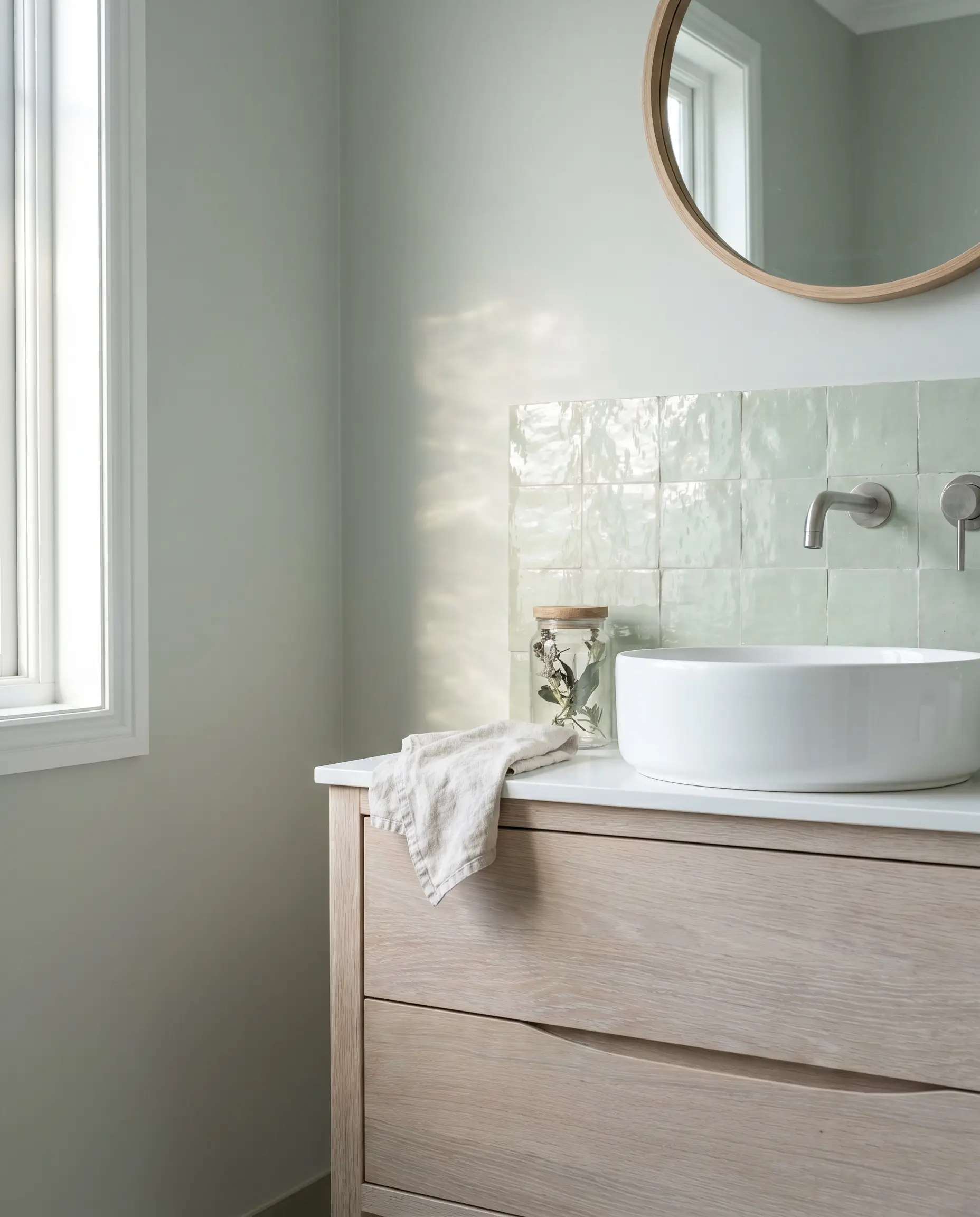 A bleached oak vanity supports a white ceramic vessel sink against a pale celadon zellige tile wall bordered by Farrow and Ball Cromarty paint.