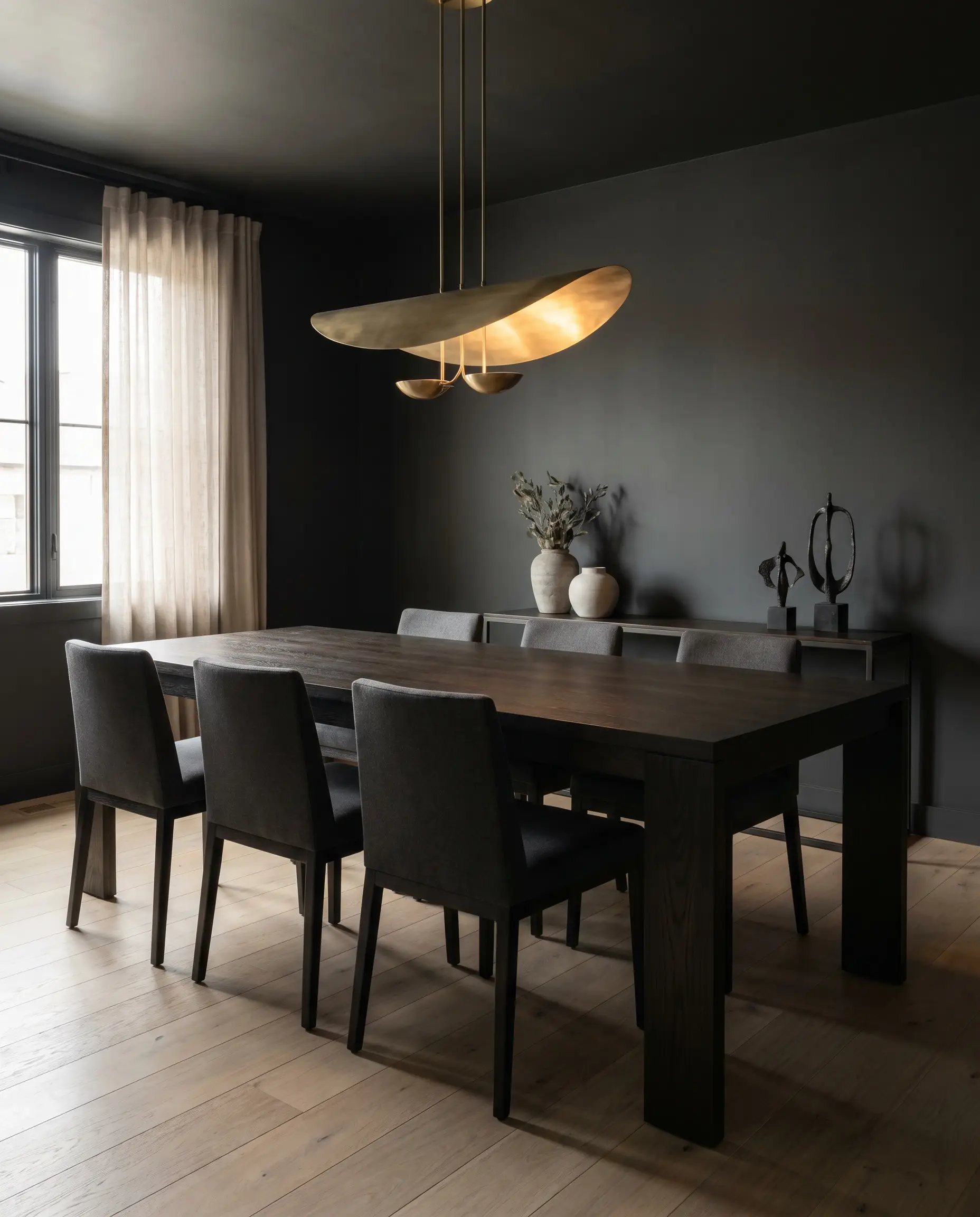 A contemporary brass pendant light illuminates a dark-stained oak dining table surrounded by Benjamin Moore Wrought Iron walls and pale European light oak planks.