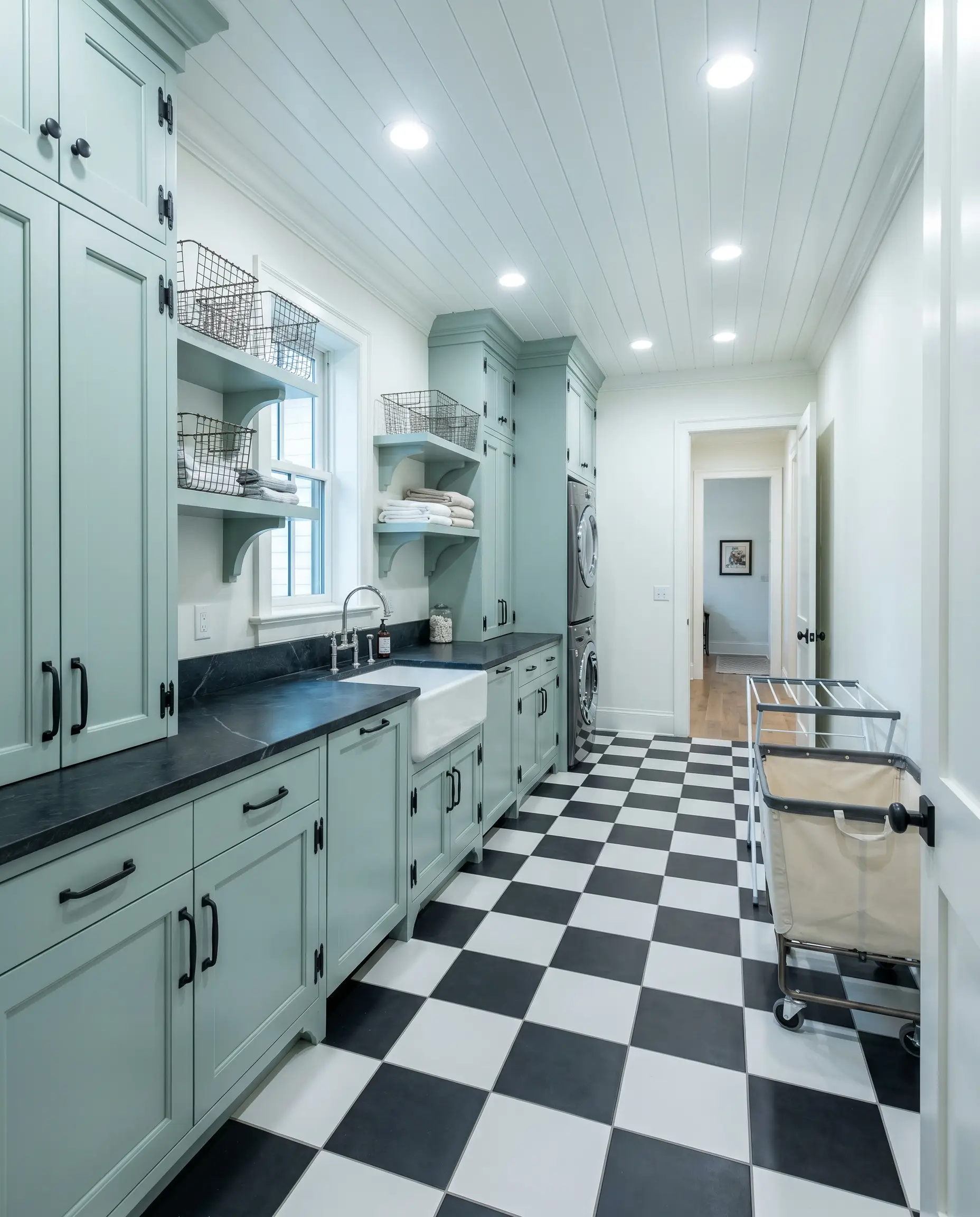 Custom built-in cabinetry painted in Benjamin Moore Palladian Blue (Hex #C1D1C9) contrasts sharply with deep charcoal soapstone countertops and a black and white checkerboard floor.
